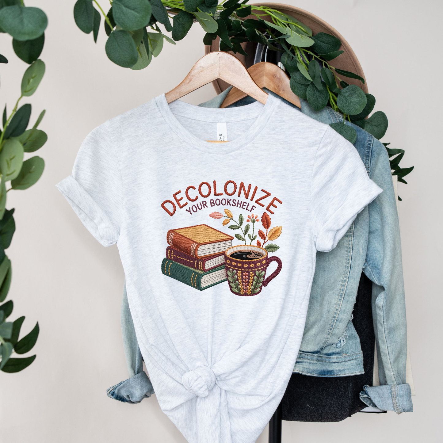 Decolonize Your Bookshelf Shirt featuring stacked books, a floral coffee mug, botanical accents, and embroidered-style lettering. decolonize your bookshelf shirt, book lover shirt, reader shirt, librarian shirt, teacher shirt, bookworm shirt, reading shirt, book club shirt, diverse books shirt, indigenous literature, bookstore shirt, coffee and books, literary shirt, reader gift, librarian gift, teacher gift, book aesthetic shirt, bookish apparel, reading enthusiast, book nerd shirt