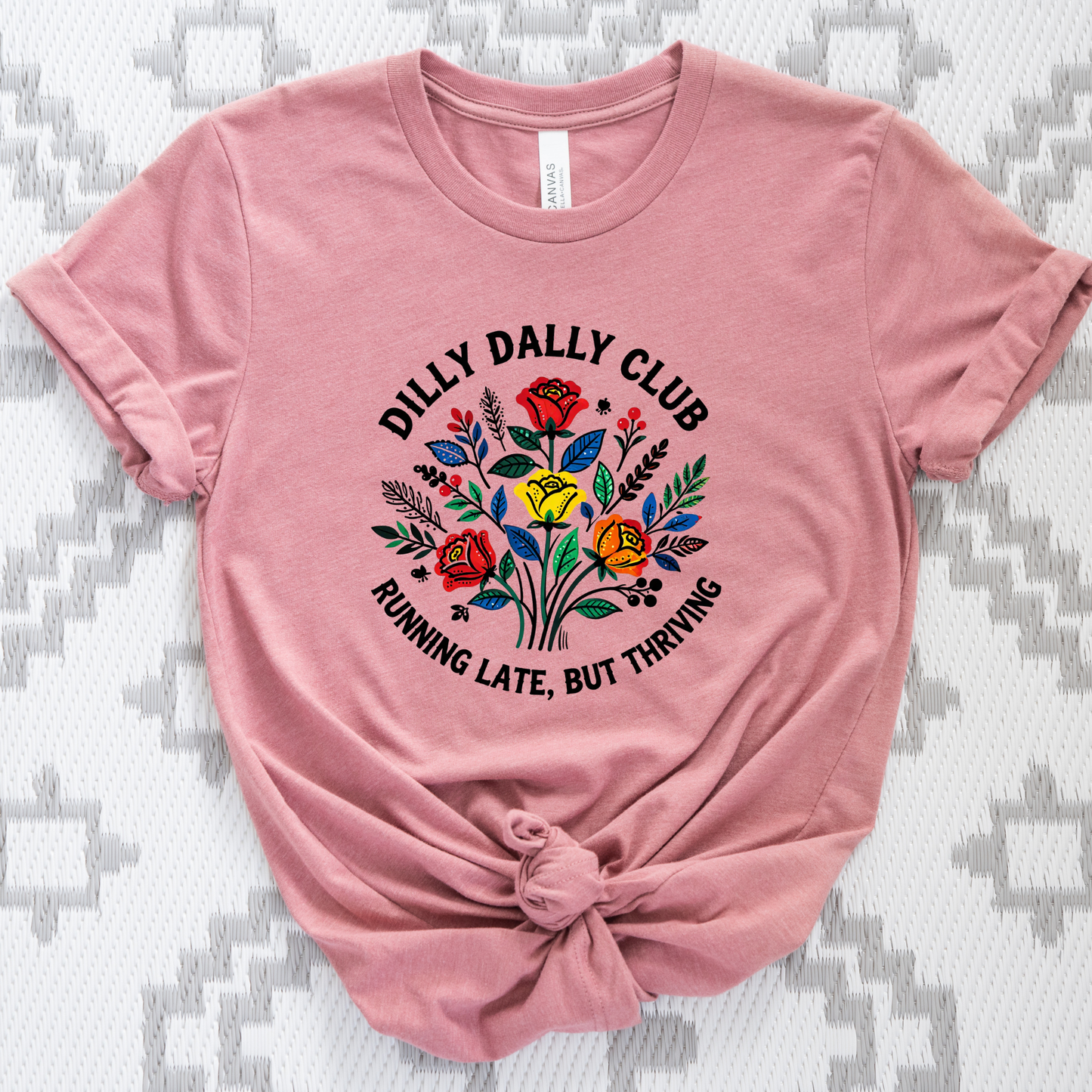 Dilly Dally Club Running Late, But Thriving shirt design featuring colorful woodland-inspired floral artwork with red, yellow, orange, blue, and green flowers arranged in a bouquet. Circular text reads 'Dilly Dally Club' and 'Running Late, But Thriving' on a transparent background. Dilly Dally Club, Running Late But Thriving, Woodland Floral, Floral Shirt, Graphic Tee, Funny Shirt, Unisex Tee, Floral Graphic Tee, Indigenous Inspired, Botanical Shirt, Cottagecore Fashion, Colorful Shirt, Gift For Her