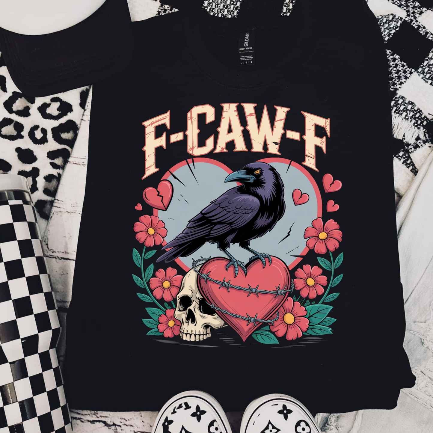 Black t-shirt with a graphic design featuring a crow, skull, and flowers on a checkered background.