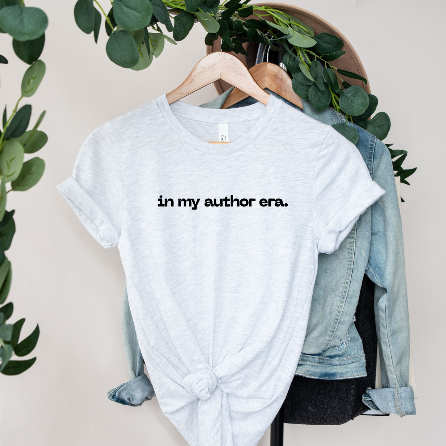 White t-shirt with 'in my author era.' text on a hanger with a denim jacket and greenery. in my author era shirt, writer shirt, author tee, writing shirt, nanowrimo shirt, book author apparel, novelist shirt, writer gift shirt, author era tee, creative writer clothing, book launch shirt, writing community tee, aspiring author shirt, fiction writer apparel, manuscript shirt