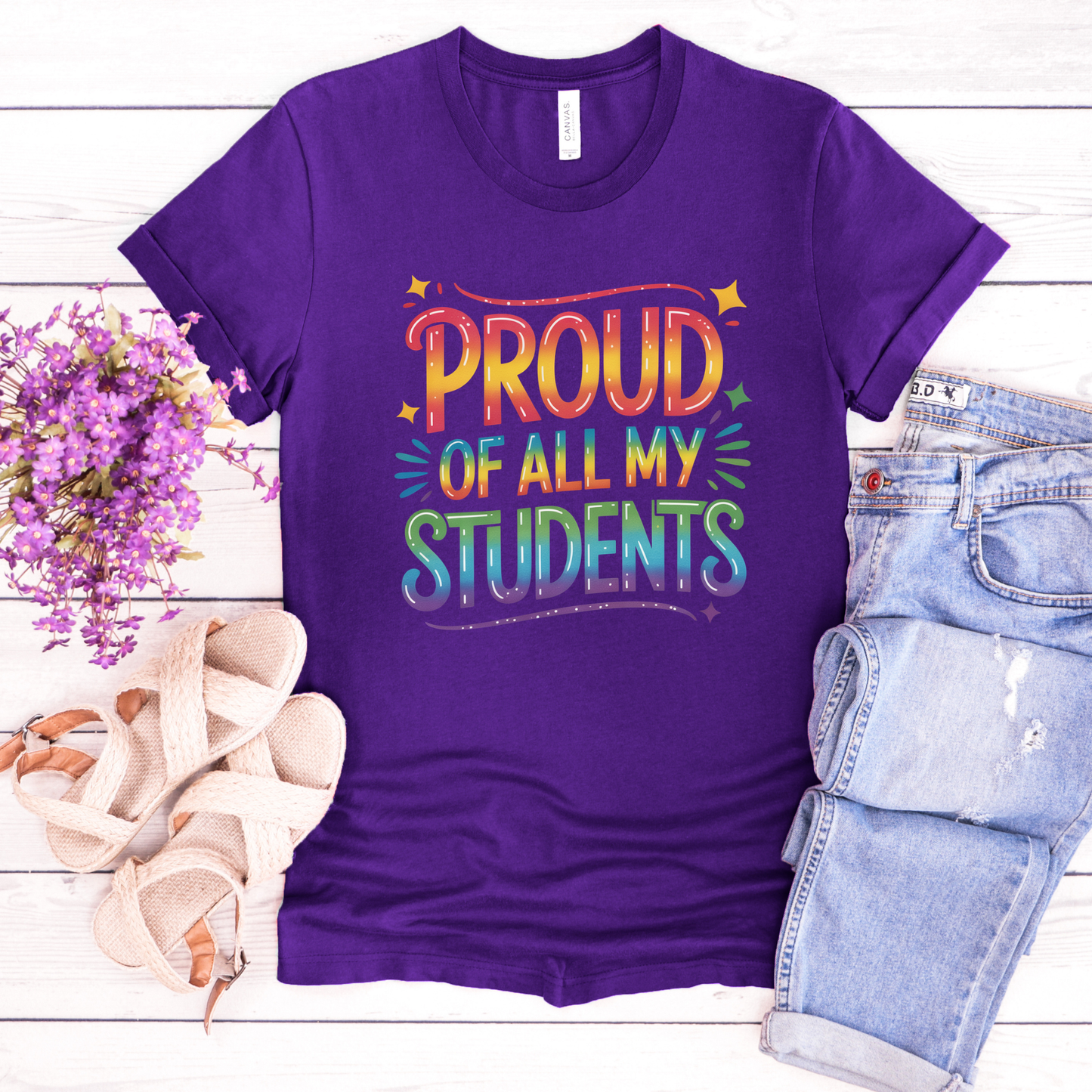 Purple t-shirt with 'Proud of all my students' text on a wooden surface with flowers and jeans. teacher pride shirt, inclusive teacher shirt, LGBTQ ally teacher gift, pride month shirt, supportive teacher apparel, equality shirt for educators, school pride clothing, safe space shirt, diversity and inclusion tee, teacher appreciation gift, back to school pride shirt, unisex teacher shirt, classroom pride outfit, LGBTQ pride clothing, positive message shirt