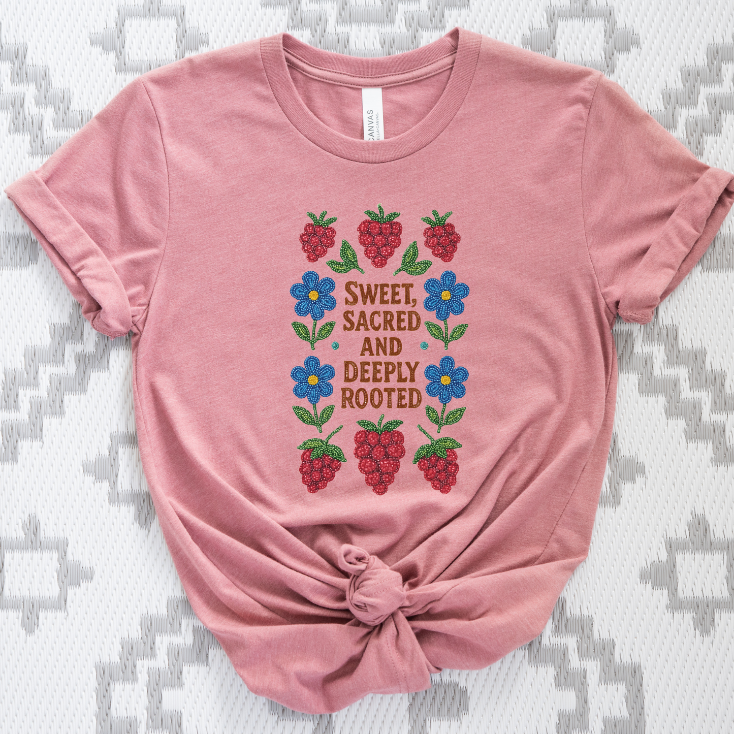 Pink t-shirt with floral and berry design on a textured surface sweet sacred deeply rooted shirt, beaded floral berry tee, indigenous beaded design shirt, sacred roots indigenous apparel, floral berry cultural t-shirt, original indigenous graphic tee, beaded indigenous shirt, deeply rooted heritage tee, unisex cultural pride shirt, sahdeh spruce indigenous design, berry beadwork t-shirt, ancestral connection apparel