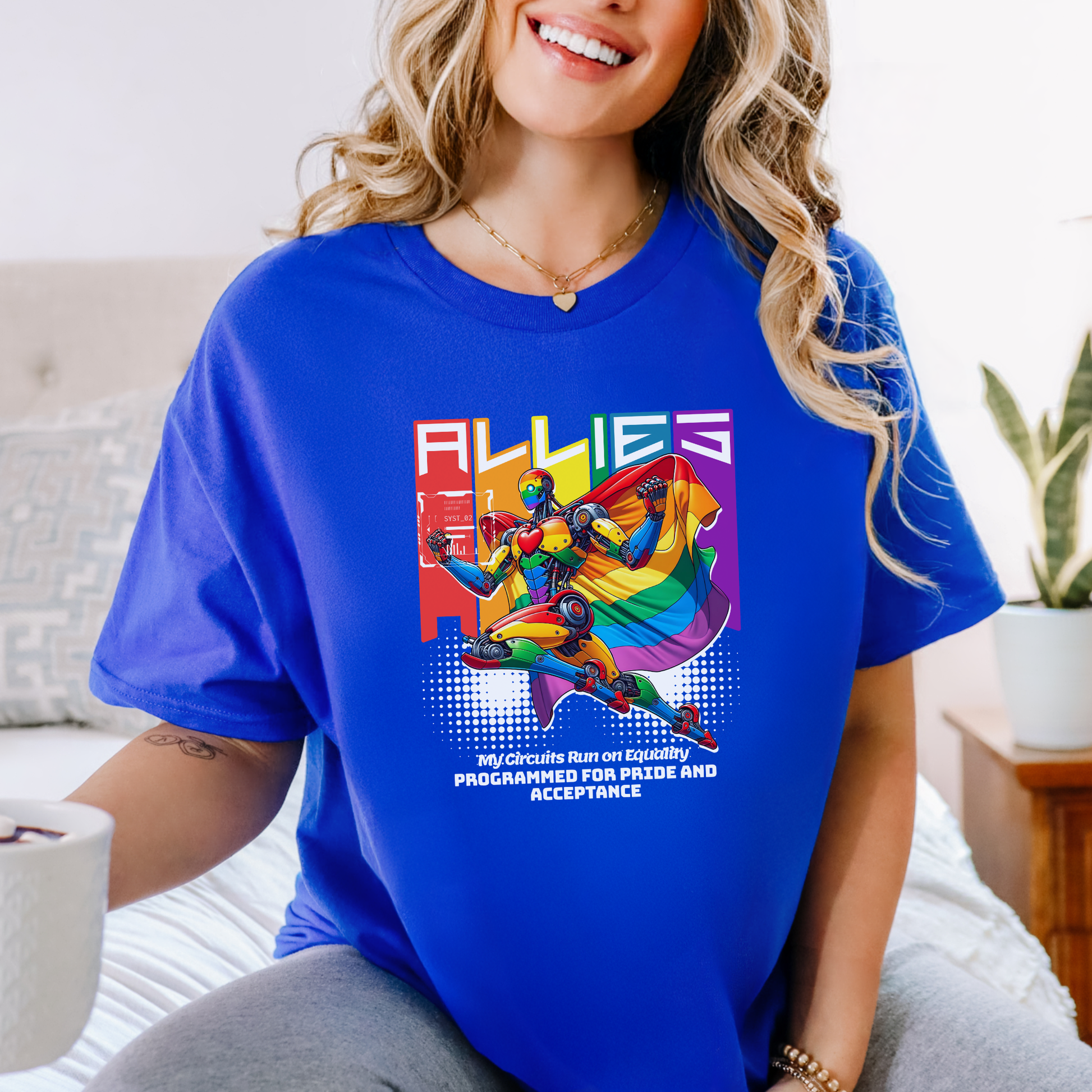 Woman wearing a blue t-shirt with a colorful graphic and text, sitting on a couch. allies robot shirt, pride shirt, ally shirt, LGBTQ support tee, rainbow graphic tee, equality shirt, acceptance shirt, unisex graphic tee, pride apparel, colorful robot shirt, statement tee, allyship apparel, inclusive fashion, fun pride shirt, rainbow ally shirt