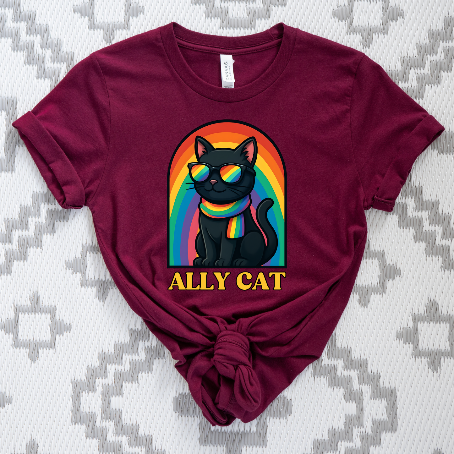 Maroon t-shirt with a colorful cat graphic and 'ALLY CAT' text on a patterned background ally cat shirt, rainbow cat shirt, LGBTQ ally shirt, pride cat tee, allyship shirt, cat lover shirt, unisex graphic tee, rainbow shirt, pride apparel, support LGBTQ, fun ally tee, colorful cat shirt, statement tee, cat graphic shirt, inclusive clothing