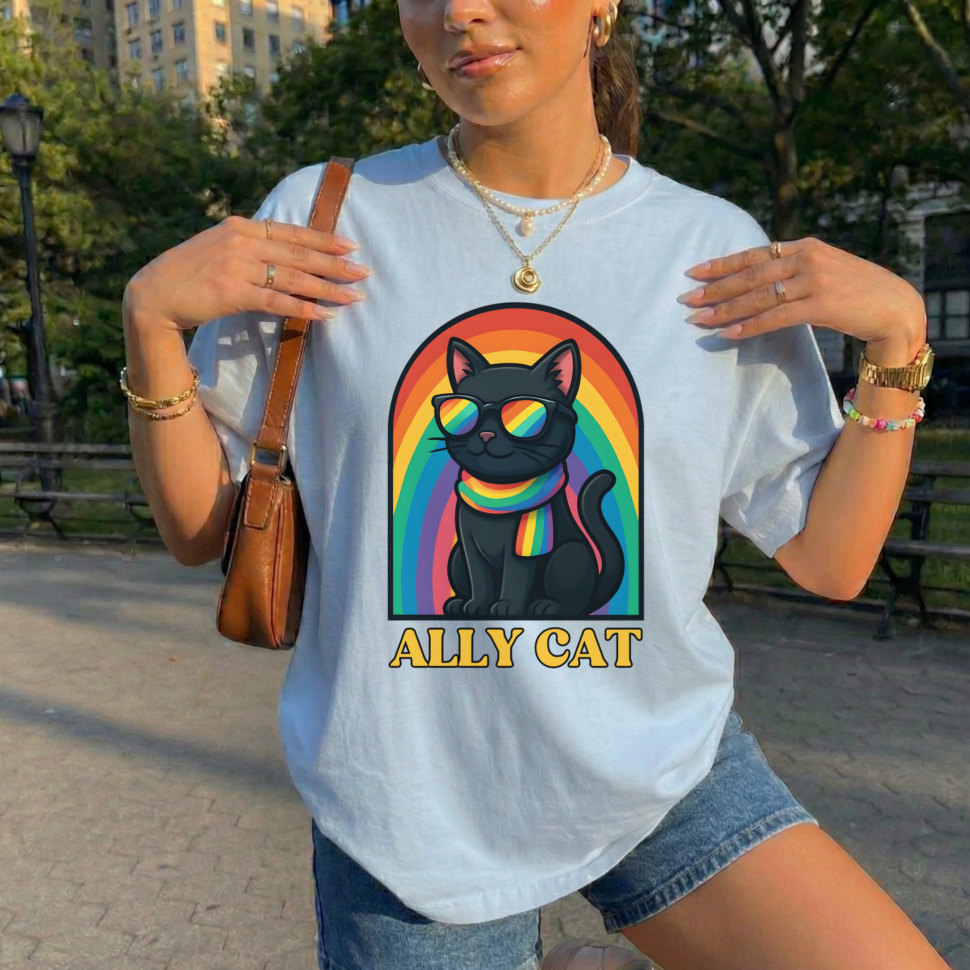 Person wearing a white t-shirt with a rainbow cat graphic and 'ALLY CAT' text in a park. ally cat shirt, rainbow cat shirt, LGBTQ ally shirt, pride cat tee, allyship shirt, cat lover shirt, unisex graphic tee, rainbow shirt, pride apparel, support LGBTQ, fun ally tee, colorful cat shirt, statement tee, cat graphic shirt, inclusive clothing