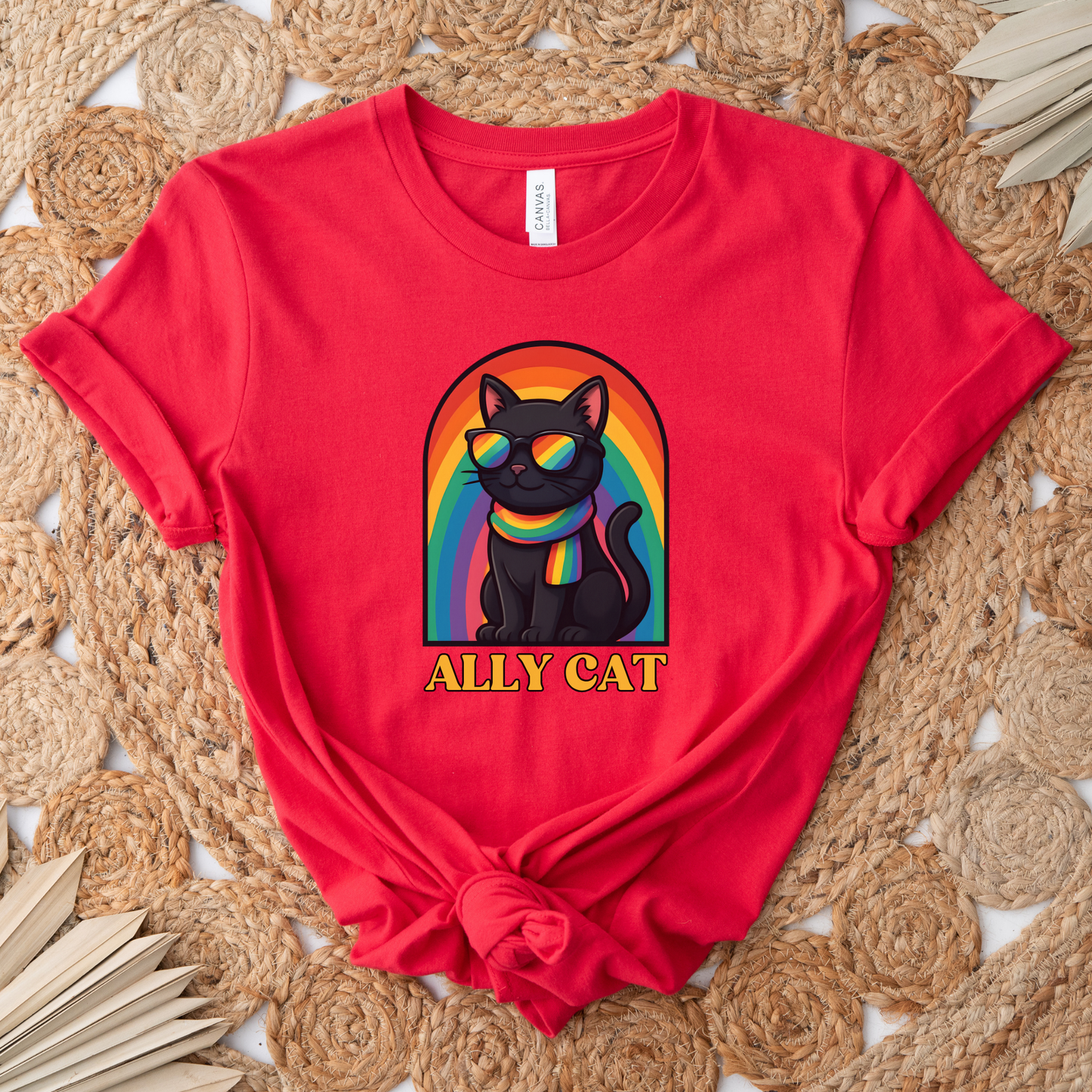 Red t-shirt with a black cat wearing a rainbow-colored collar and 'ALLY CAT' text on a woven mat background. ally cat shirt, rainbow cat shirt, LGBTQ ally shirt, pride cat tee, allyship shirt, cat lover shirt, unisex graphic tee, rainbow shirt, pride apparel, support LGBTQ, fun ally tee, colorful cat shirt, statement tee, cat graphic shirt, inclusive clothing