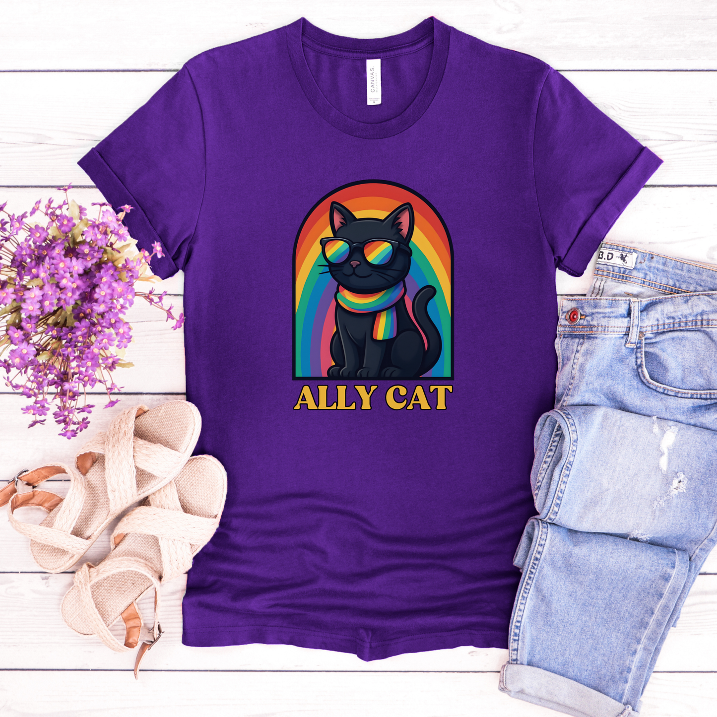 Purple t-shirt with a black cat wearing rainbow sunglasses and a rainbow arch, labeled 'ALLY CAT', on a wooden surface with flowers and shorts. ally cat shirt, rainbow cat shirt, LGBTQ ally shirt, pride cat tee, allyship shirt, cat lover shirt, unisex graphic tee, rainbow shirt, pride apparel, support LGBTQ, fun ally tee, colorful cat shirt, statement tee, cat graphic shirt, inclusive clothing