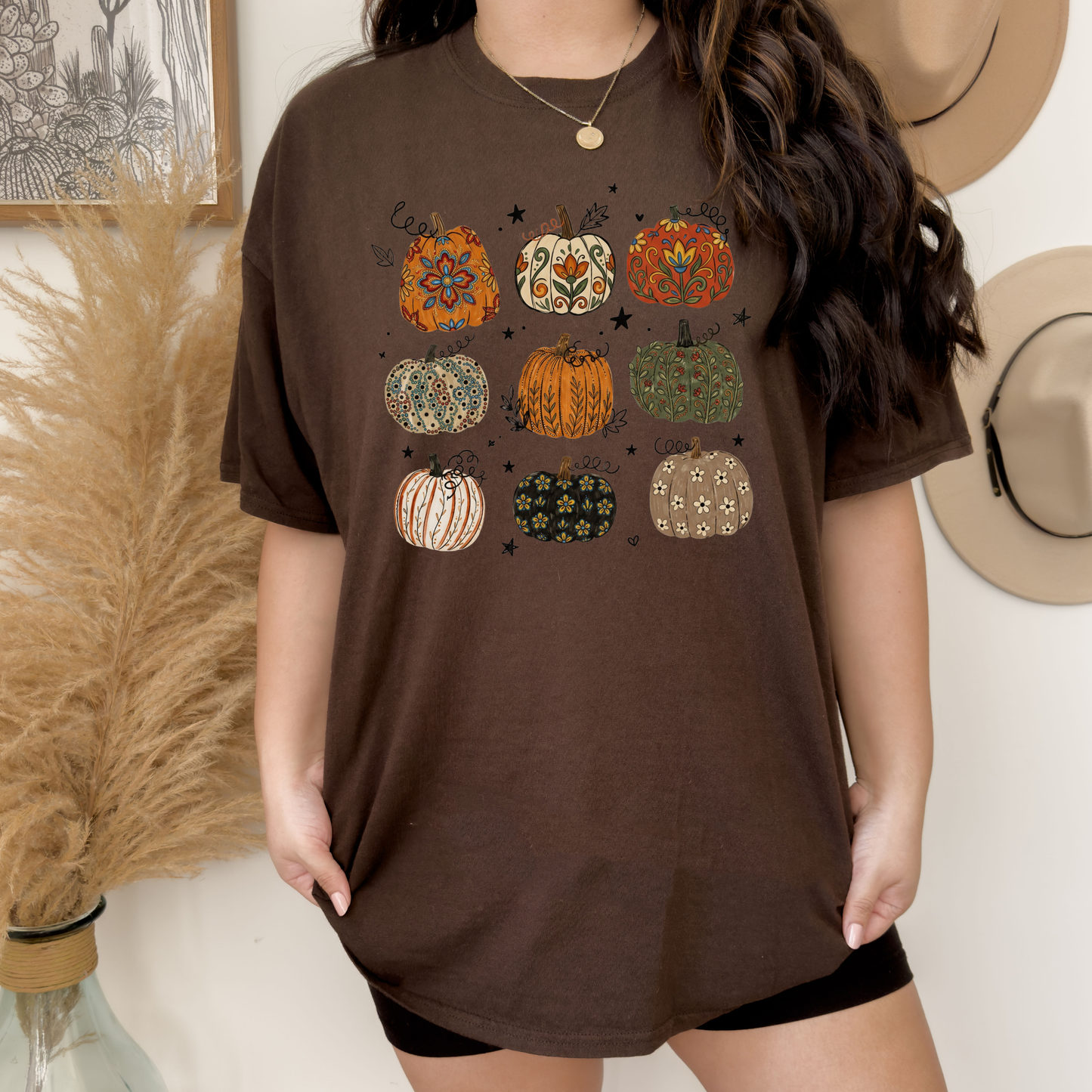 t-shirt featuring nine decorative pumpkins with Indigenous-inspired floral and botanical patterns in warm autumn colors arranged in a grid. indigenous pumpkin shirt, boho pumpkin shirt, fall pumpkin shirt, autumn graphic tee, thanksgiving shirt, indigenous inspired shirt, floral pumpkin shirt, woodland fall shirt, pumpkin patch outfit, harvest shirt, boho fall fashion, cozy autumn tee, fall aesthetic shirt, pumpkin lover gift, autumn apparel, cottagecore fall shirt, botanical pumpkin shirt