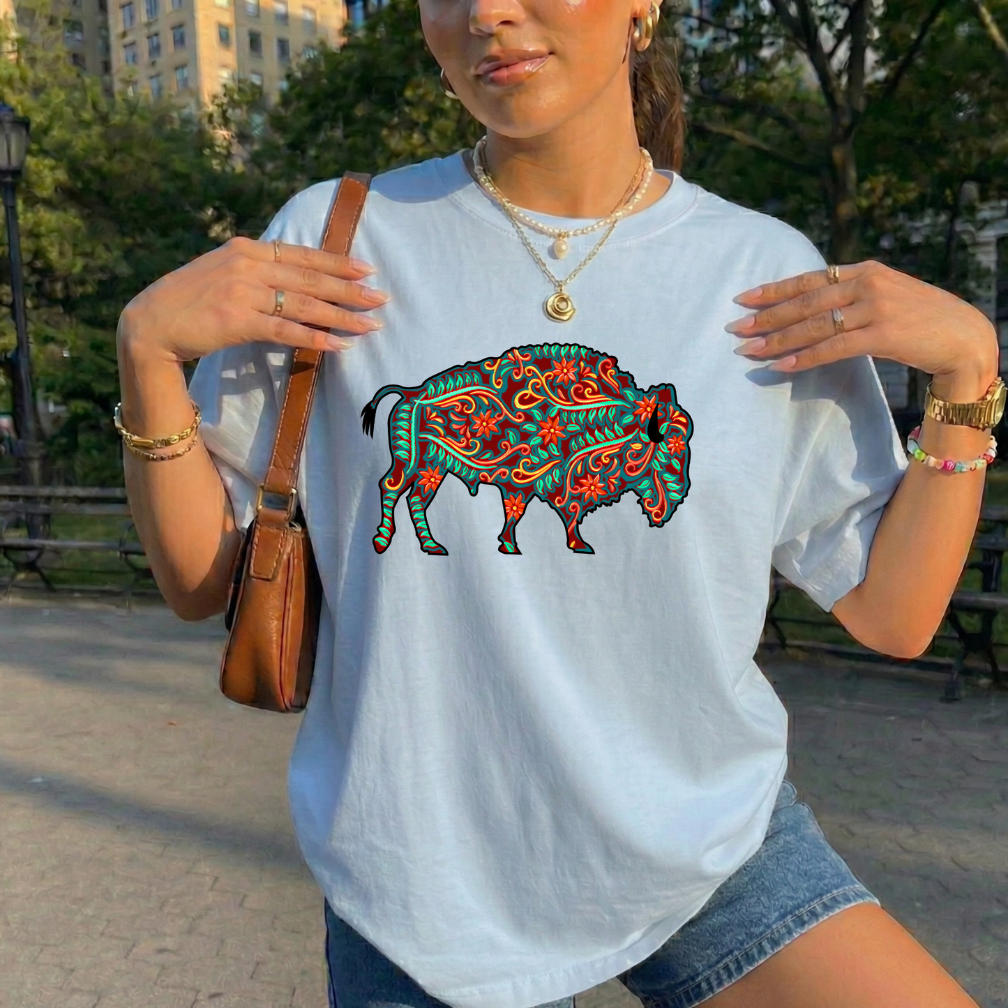Person wearing a white t-shirt with a colorful bull graphic in an outdoor setting. native floral buffalo shirt, indigenous buffalo shirt, floral buffalo tee, indigenous design shirt, buffalo graphic tee, native inspired apparel, cultural pride shirt, unisex indigenous tee, floral indigenous shirt, buffalo and floral shirt, indigenous owned clothing, meaningful graphic tee