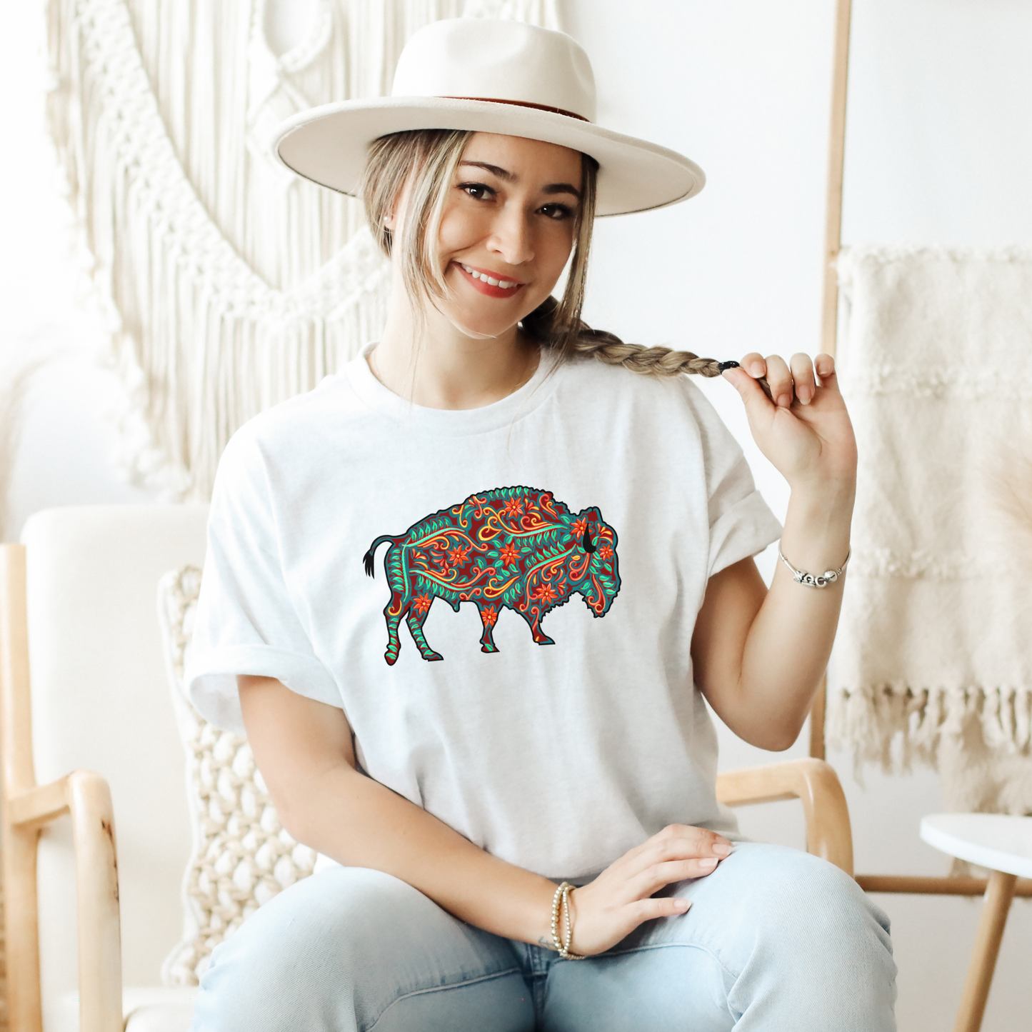 Woman wearing a white t-shirt with a colorful buffalo design, sitting in a cozy room. native floral buffalo shirt, indigenous buffalo shirt, floral buffalo tee, indigenous design shirt, buffalo graphic tee, native inspired apparel, cultural pride shirt, unisex indigenous tee, floral indigenous shirt, buffalo and floral shirt, indigenous owned clothing, meaningful graphic tee