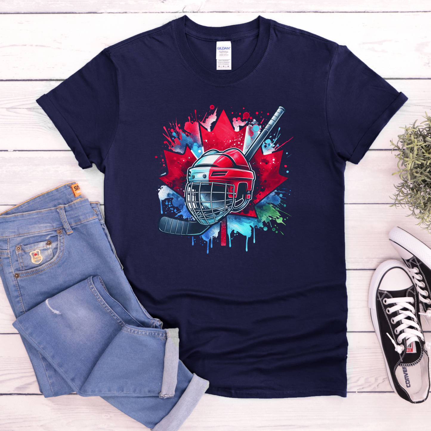 Canada Hockey Shirt featuring a colorful hockey helmet and stick graphic layered over a vibrant red Canadian maple leaf with paint splash accents. Proudly made in Canada, this patriotic hockey t-shirt is perfect for hockey fans, players, coaches, and Canada Day celebrations.