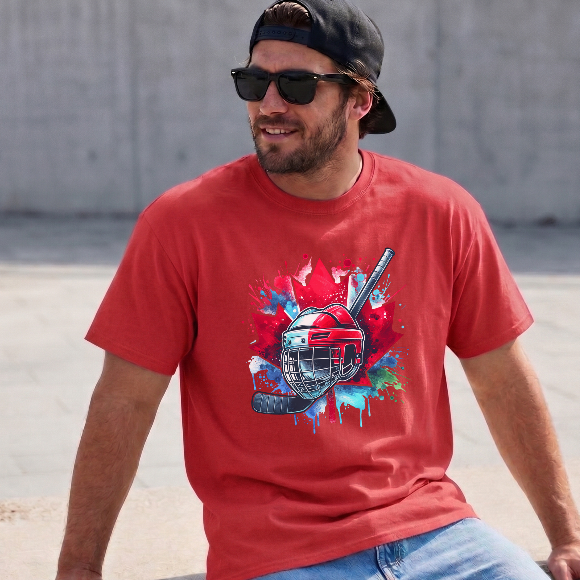 Canada Hockey Shirt featuring a colorful hockey helmet and stick graphic layered over a vibrant red Canadian maple leaf with paint splash accents. Proudly made in Canada, this patriotic hockey t-shirt is perfect for hockey fans, players, coaches, and Canada Day celebrations.