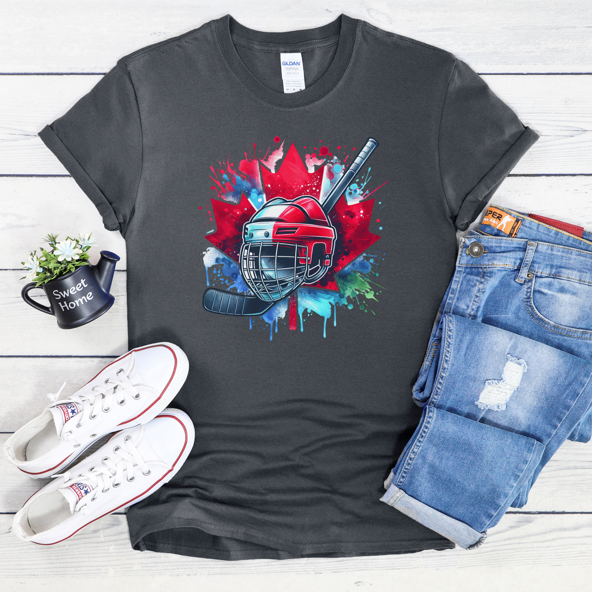 Canada Hockey Shirt featuring a colorful hockey helmet and stick graphic layered over a vibrant red Canadian maple leaf with paint splash accents. Proudly made in Canada, this patriotic hockey t-shirt is perfect for hockey fans, players, coaches, and Canada Day celebrations.