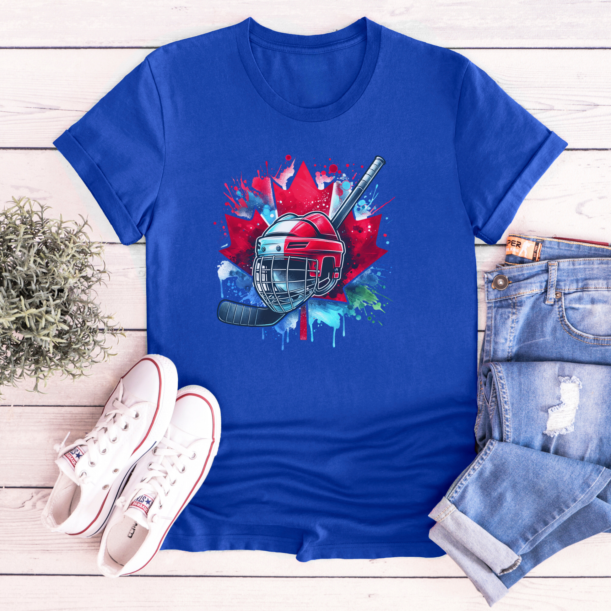 Canada Hockey Shirt featuring a colorful hockey helmet and stick graphic layered over a vibrant red Canadian maple leaf with paint splash accents. Proudly made in Canada, this patriotic hockey t-shirt is perfect for hockey fans, players, coaches, and Canada Day celebrations.