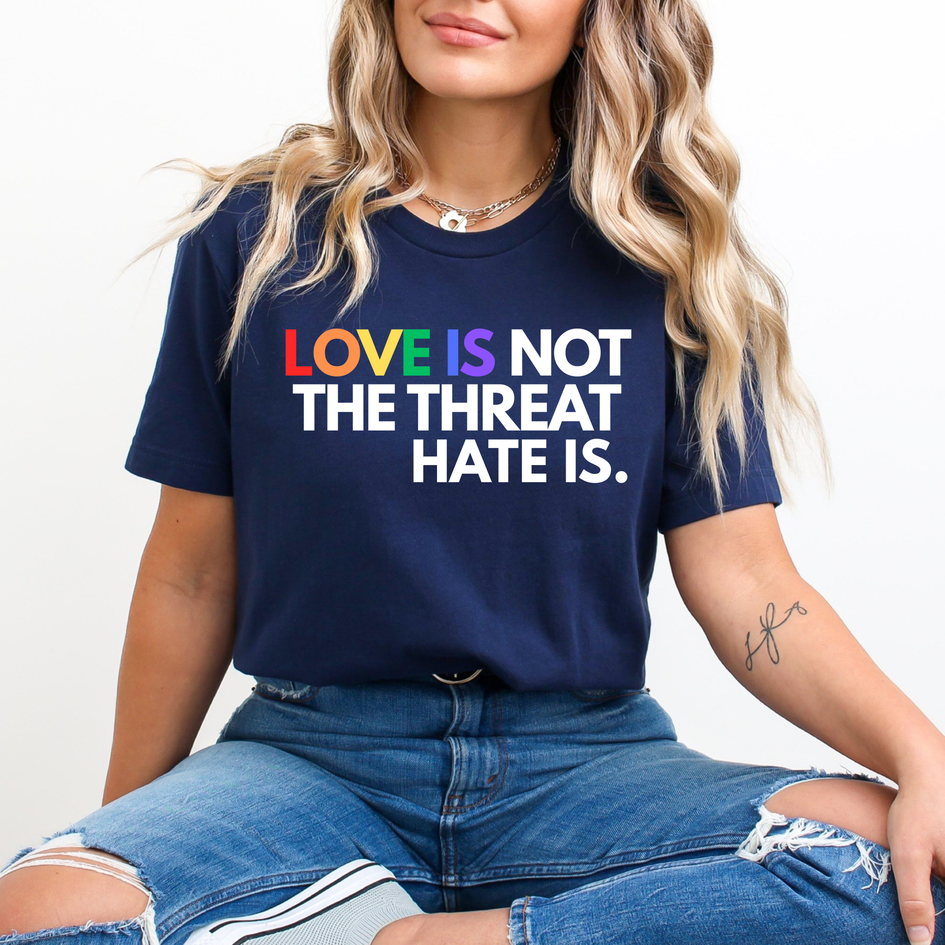 t-shirt featuring the phrase "Love Is Not The Threat Hate Is." with rainbow-colored lettering for Love, promoting LGBTQ+ pride, equality, and inclusion. love is not the threat hate is shirt, pride shirt, pride ally shirt, LGBTQ shirt, LGBTQ ally, equality shirt, love wins shirt, rainbow shirt, inclusive apparel, human rights shirt, kindness shirt, acceptance shirt, pride month shirt, ally gift, social justice shirt, equality tee, progressive apparel, support LGBTQ, activist shirt, inclusive graphic tee