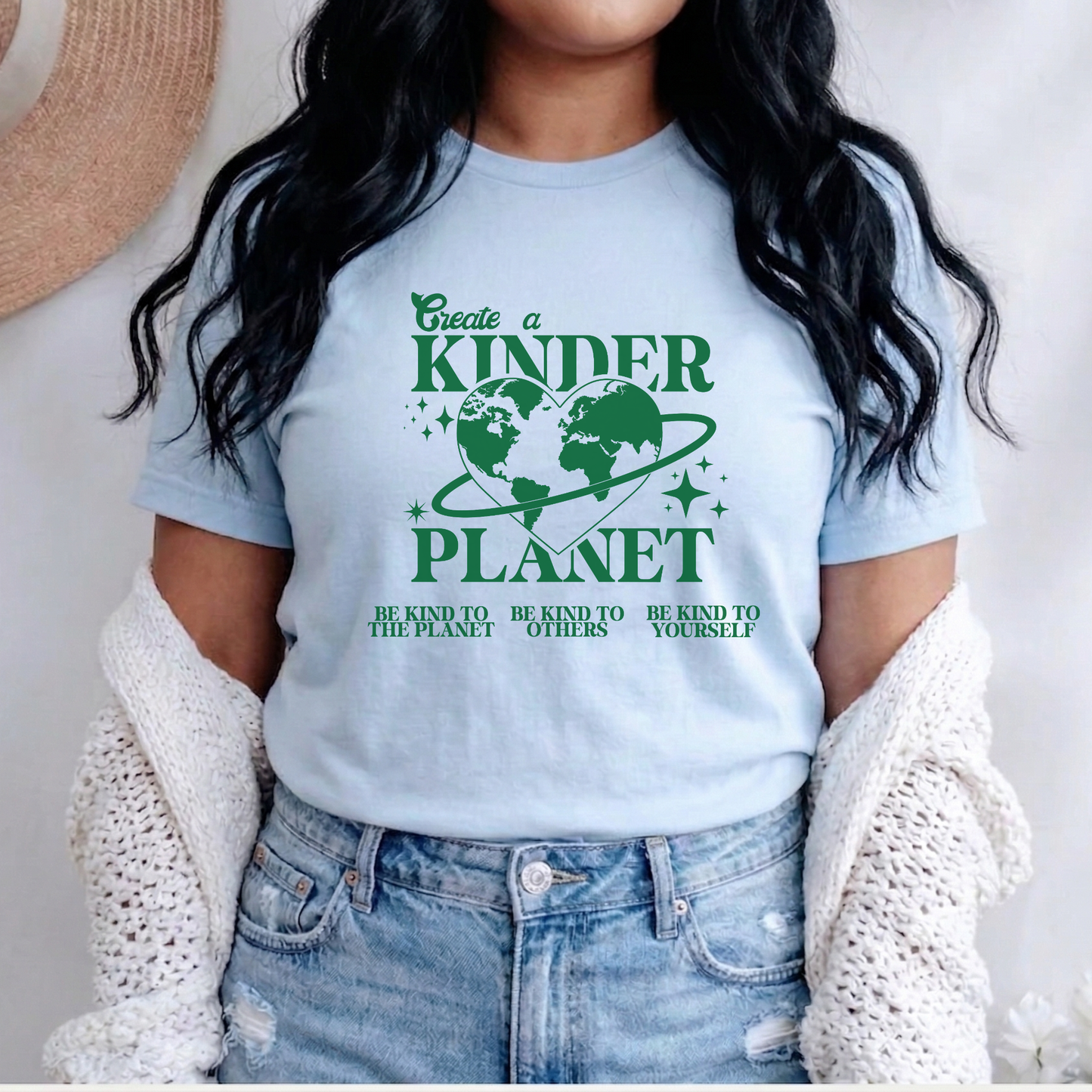 Person wearing a light blue t-shirt with a green environmental message design. Create A Kinder Planet, kinder planet shirt, kindness tee, eco awareness shirt, compassionate clothing, unisex graphic tee, environmental activism, positive change shirt, family eco tee, sustainable fashion, Indigenous brand, uplifting apparel, earth kindness, statement t-shirt, motivational tee