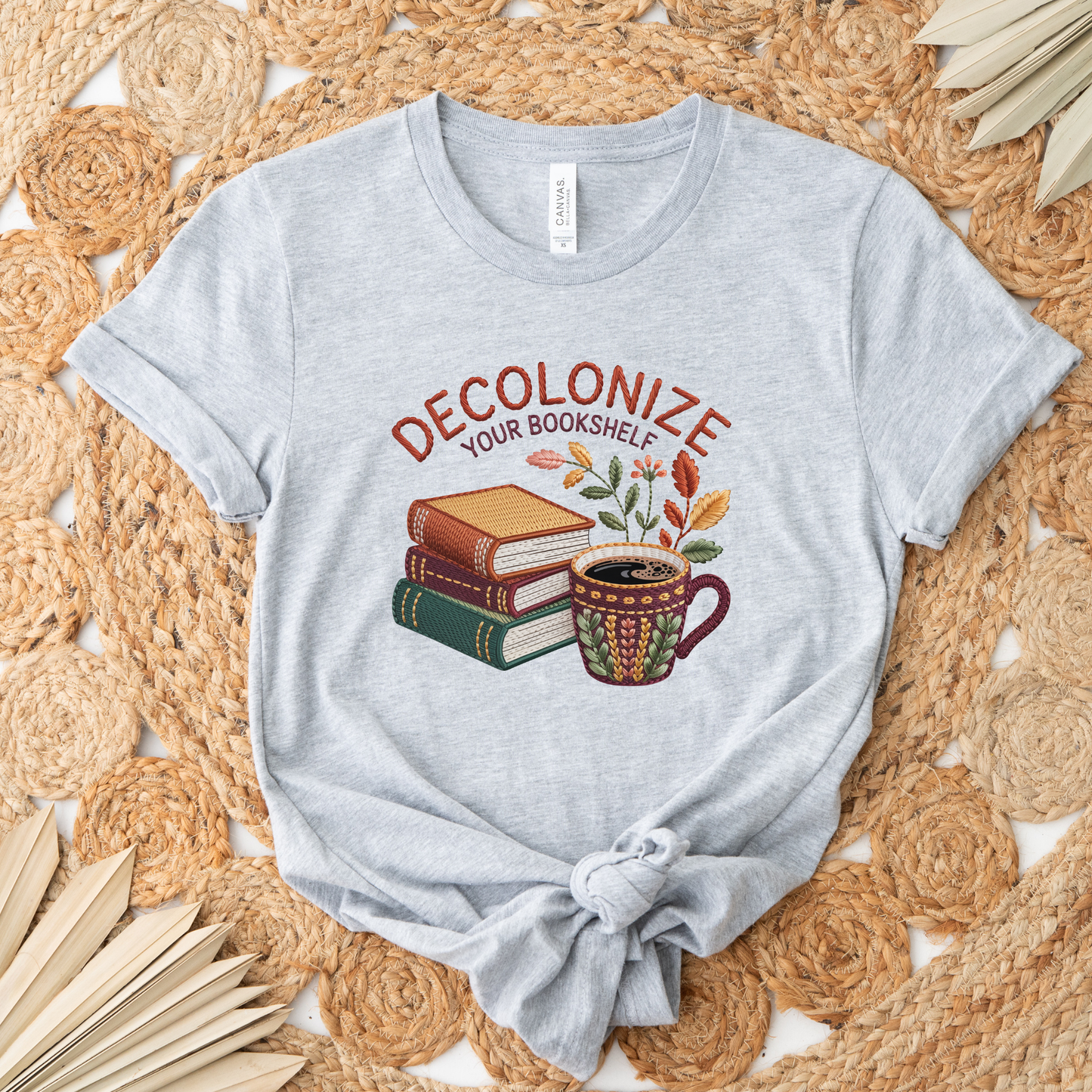 Decolonize Your Bookshelf Shirt featuring stacked books, a floral coffee mug, botanical accents, and embroidered-style lettering. decolonize your bookshelf shirt, book lover shirt, reader shirt, librarian shirt, teacher shirt, bookworm shirt, reading shirt, book club shirt, diverse books shirt, indigenous literature, bookstore shirt, coffee and books, literary shirt, reader gift, librarian gift, teacher gift, book aesthetic shirt, bookish apparel, reading enthusiast, book nerd shirt