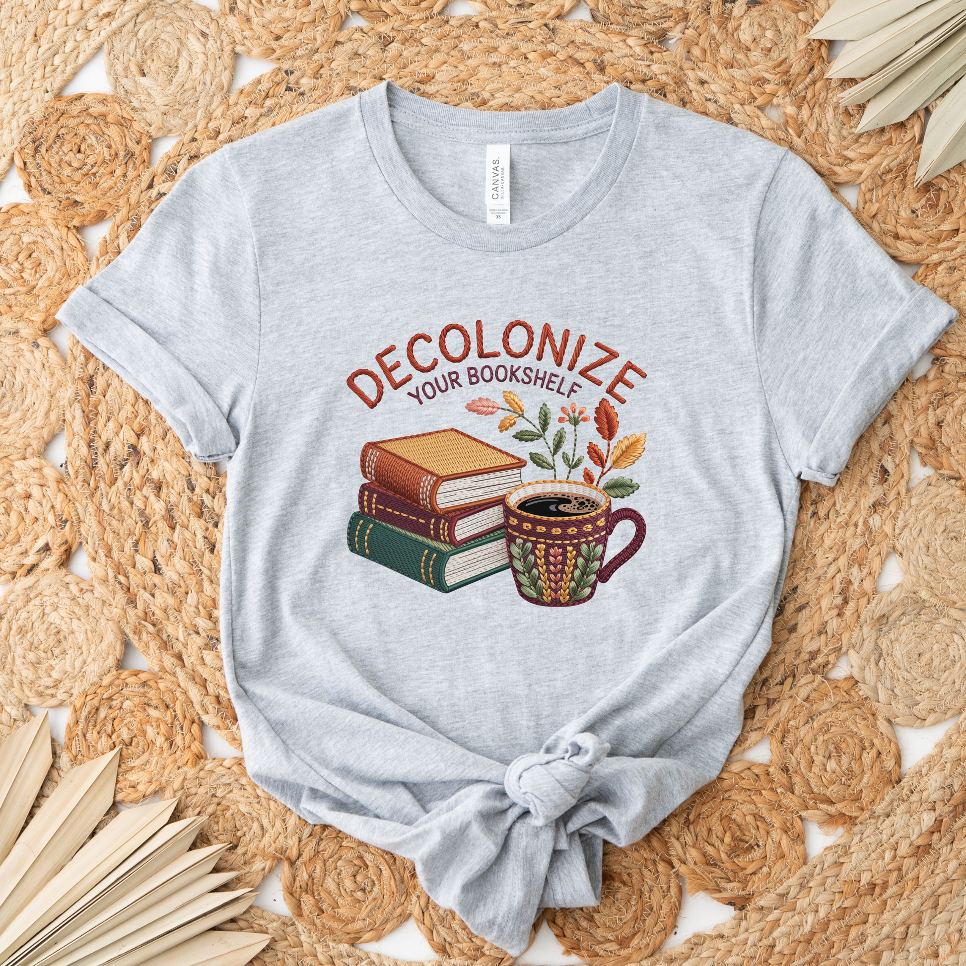 Decolonize Your Bookshelf Shirt featuring stacked books, a floral coffee mug, botanical accents, and embroidered-style lettering. decolonize your bookshelf shirt, book lover shirt, reader shirt, librarian shirt, teacher shirt, bookworm shirt, reading shirt, book club shirt, diverse books shirt, indigenous literature, bookstore shirt, coffee and books, literary shirt, reader gift, librarian gift, teacher gift, book aesthetic shirt, bookish apparel, reading enthusiast, book nerd shirt