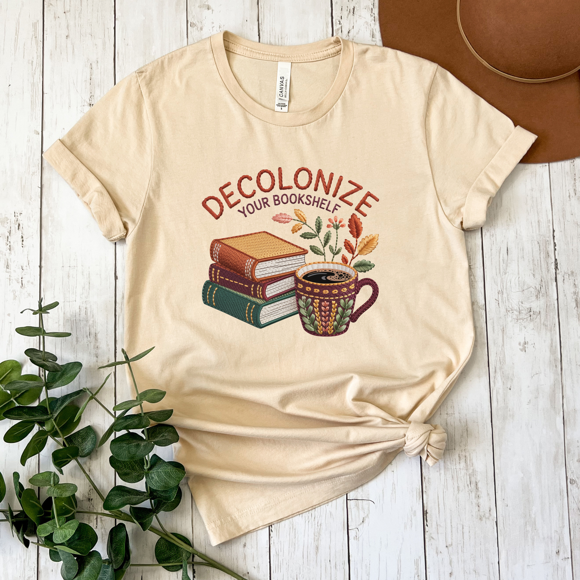 Decolonize Your Bookshelf Shirt featuring stacked books, a floral coffee mug, botanical accents, and embroidered-style lettering. decolonize your bookshelf shirt, book lover shirt, reader shirt, librarian shirt, teacher shirt, bookworm shirt, reading shirt, book club shirt, diverse books shirt, indigenous literature, bookstore shirt, coffee and books, literary shirt, reader gift, librarian gift, teacher gift, book aesthetic shirt, bookish apparel, reading enthusiast, book nerd shirt