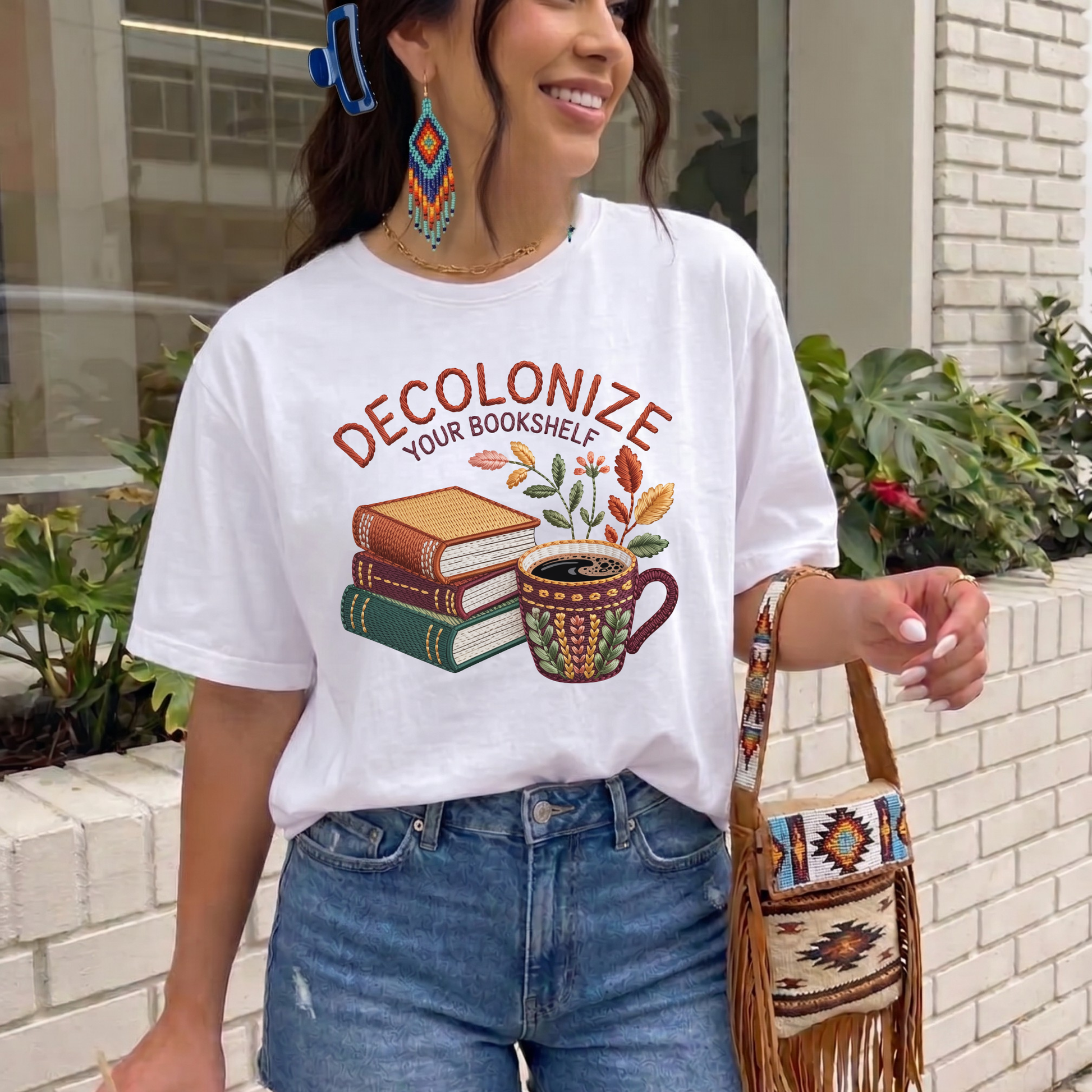 Decolonize Your Bookshelf Shirt featuring stacked books, a floral coffee mug, botanical accents, and embroidered-style lettering. decolonize your bookshelf shirt, book lover shirt, reader shirt, librarian shirt, teacher shirt, bookworm shirt, reading shirt, book club shirt, diverse books shirt, indigenous literature, bookstore shirt, coffee and books, literary shirt, reader gift, librarian gift, teacher gift, book aesthetic shirt, bookish apparel, reading enthusiast, book nerd shirt