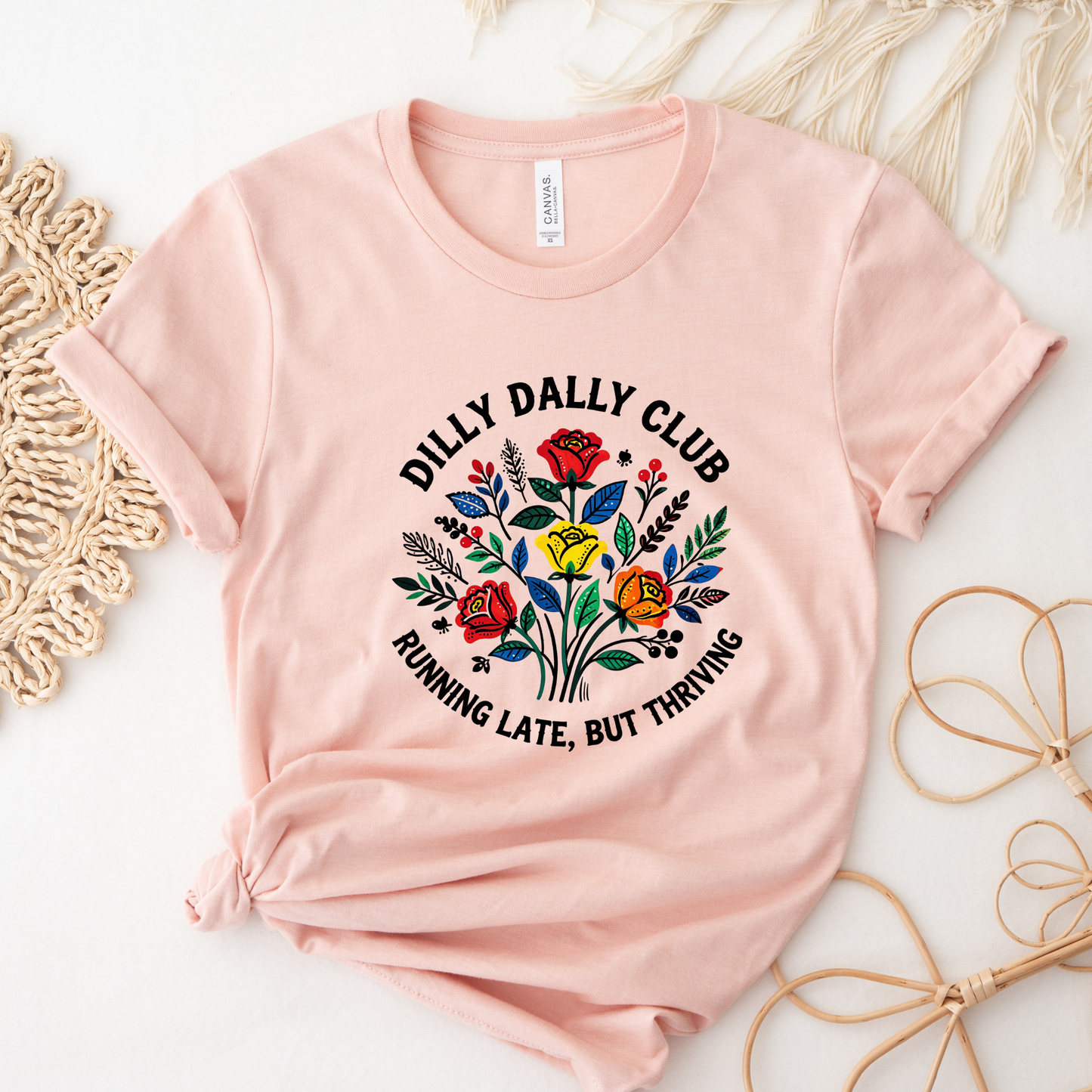Dilly Dally Club Running Late, But Thriving shirt design featuring colorful woodland-inspired floral artwork with red, yellow, orange, blue, and green flowers arranged in a bouquet. Circular text reads 'Dilly Dally Club' and 'Running Late, But Thriving' on a transparent background. Dilly Dally Club, Running Late But Thriving, Woodland Floral, Floral Shirt, Graphic Tee, Funny Shirt, Unisex Tee, Floral Graphic Tee, Indigenous Inspired, Botanical Shirt, Cottagecore Fashion, Colorful Shirt, Gift For Her