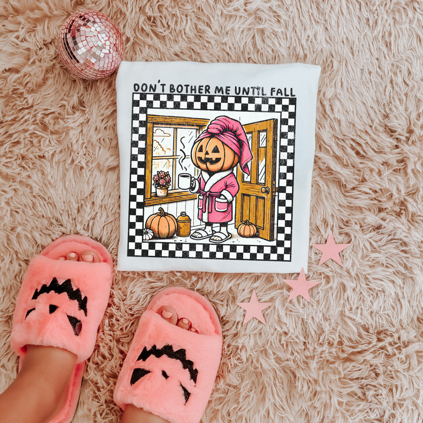 t-shirt featuring a cozy pumpkin character wearing a pink robe and towel, holding a coffee mug with the phrase "Don't Bother Me Until Fall," surrounded by autumn-inspired details and a checkered border. don't bother me until fall shirt, halloween pumpkin shirt, cozy autumn tee, fall lover t-shirt, pumpkin spice season shirt, spooky season apparel, cute pumpkin graphic tee, halloween aesthetic clothing, autumn lover gift, fall festival shirt, pumpkin patch outfit, cozy season clothing, spooky cute graphic te