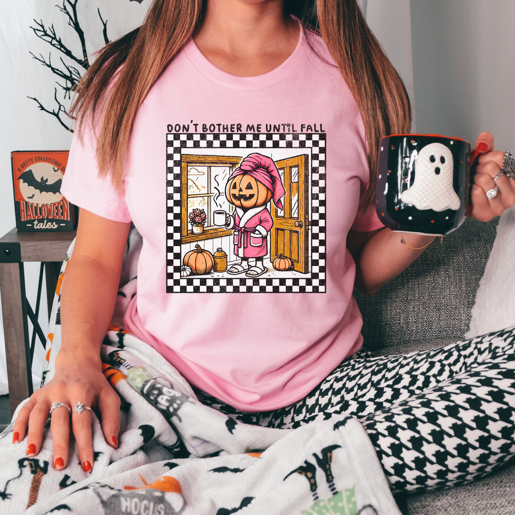 t-shirt featuring a cozy pumpkin character wearing a pink robe and towel, holding a coffee mug with the phrase "Don't Bother Me Until Fall," surrounded by autumn-inspired details and a checkered border. don't bother me until fall shirt, halloween pumpkin shirt, cozy autumn tee, fall lover t-shirt, pumpkin spice season shirt, spooky season apparel, cute pumpkin graphic tee, halloween aesthetic clothing, autumn lover gift, fall festival shirt, pumpkin patch outfit, cozy season clothing, spooky cute graphic te