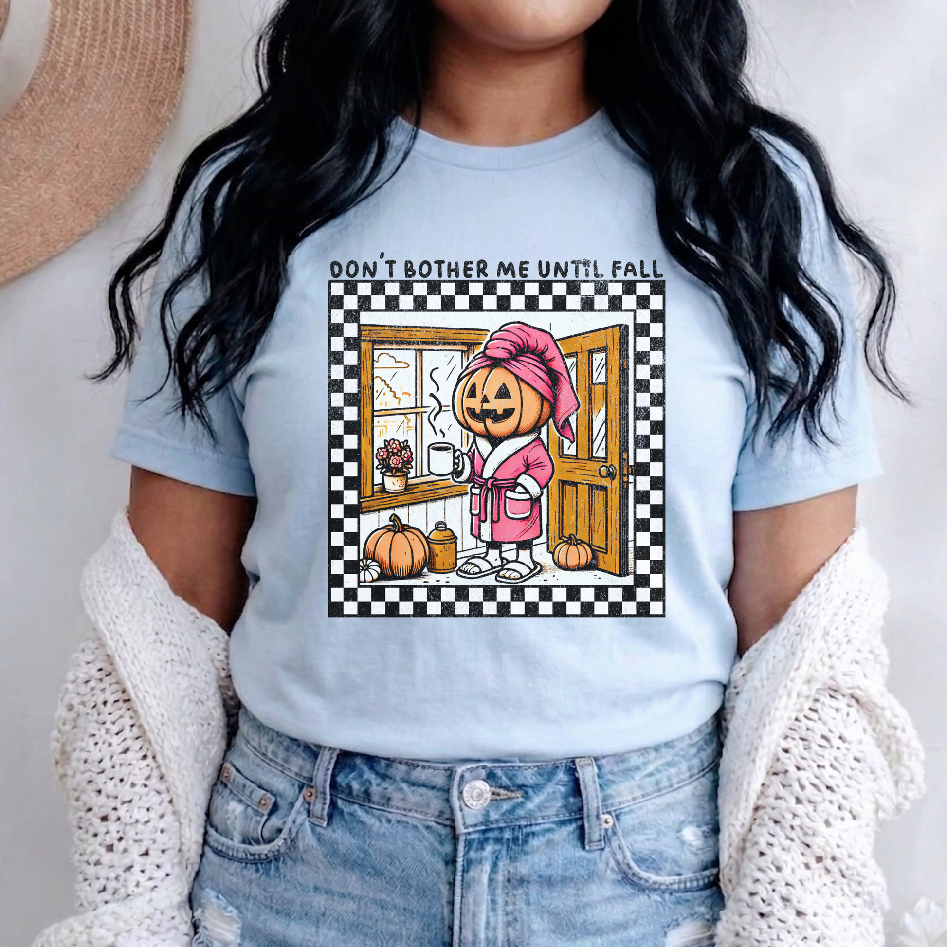 t-shirt featuring a cozy pumpkin character wearing a pink robe and towel, holding a coffee mug with the phrase "Don't Bother Me Until Fall," surrounded by autumn-inspired details and a checkered border. don't bother me until fall shirt, halloween pumpkin shirt, cozy autumn tee, fall lover t-shirt, pumpkin spice season shirt, spooky season apparel, cute pumpkin graphic tee, halloween aesthetic clothing, autumn lover gift, fall festival shirt, pumpkin patch outfit, cozy season clothing, spooky cute graphic te