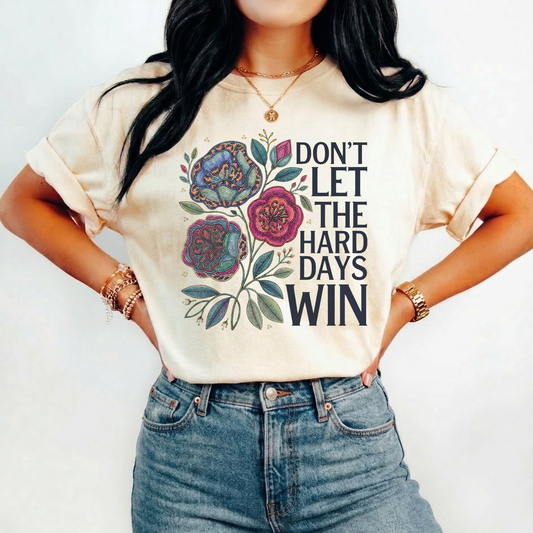 Person wearing a t-shirt with floral design and motivational quote on a plain background dont let the hard days win, inspirational shirt, motivational tee, floral graphic tee, unisex t shirt, positive quote shirt, resilience shirt, encouragement shirt, statement tee, uplifting apparel, gift idea shirt, everyday graphic tee, women’s inspirational shirt, hope shirt, feel good clothing