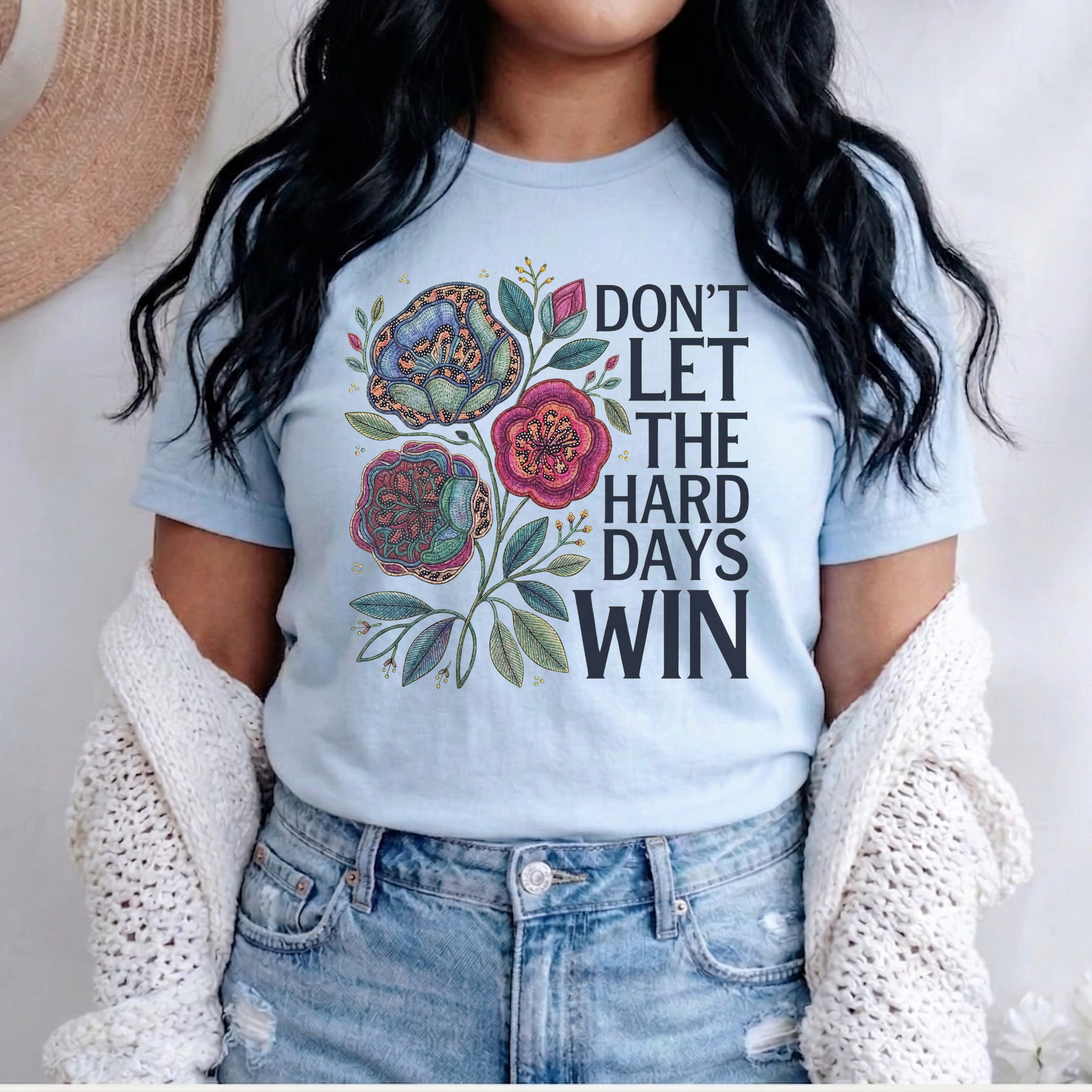 Person wearing a light blue t-shirt with floral design and text, standing against a neutral background. dont let the hard days win, inspirational shirt, motivational tee, floral graphic tee, unisex t shirt, positive quote shirt, resilience shirt, encouragement shirt, statement tee, uplifting apparel, gift idea shirt, everyday graphic tee, women’s inspirational shirt, hope shirt, feel good clothing