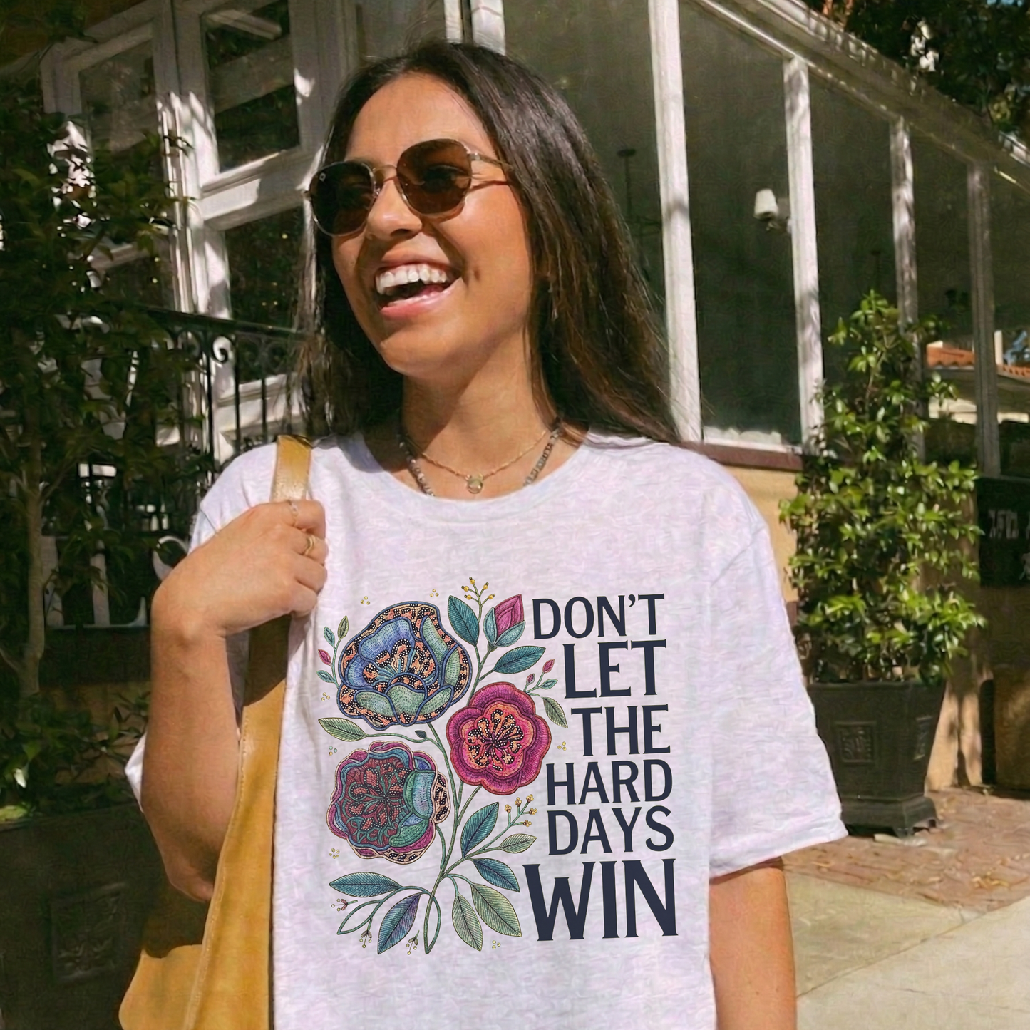 Woman wearing a t-shirt with floral design and text outdoors. dont let the hard days win, inspirational shirt, motivational tee, floral graphic tee, unisex t shirt, positive quote shirt, resilience shirt, encouragement shirt, statement tee, uplifting apparel, gift idea shirt, everyday graphic tee, women’s inspirational shirt, hope shirt, feel good clothing