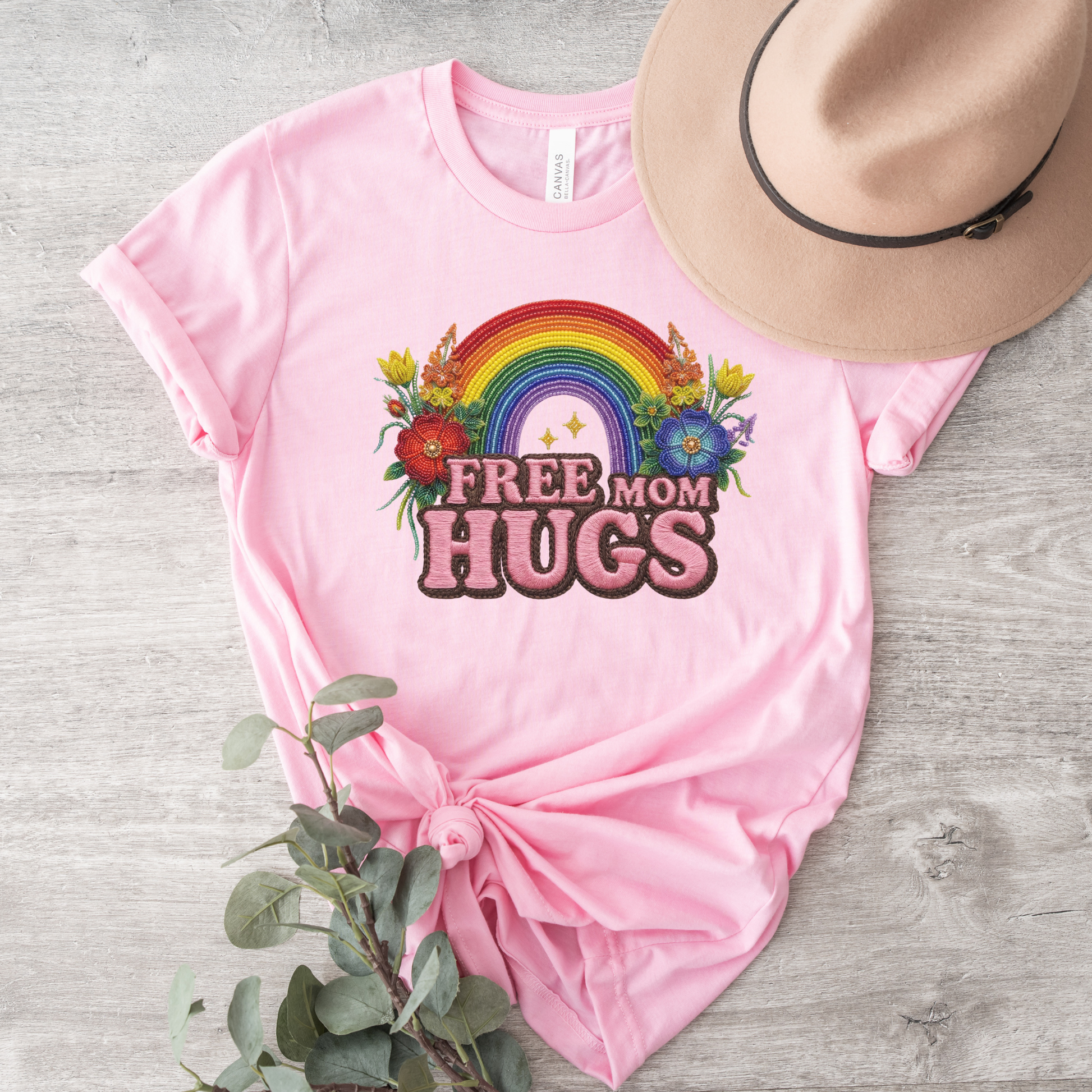 Free Mom Hugs Shirt featuring Indigenous-inspired beaded floral artwork, rainbow design, and pink faux embroidered lettering. free mom hugs shirt, pride shirt, indigenous floral shirt, beaded floral shirt, rainbow pride shirt, lgbtq ally shirt, supportive mom shirt, pride parade shirt, indigenous inspired apparel, faux embroidery shirt, mom hugs shirt, rainbow floral tee, inclusive apparel, pride month shirt, indigenous beadwork design, ally gift, lgbtq support shirt, community love shirt, acceptance shirt