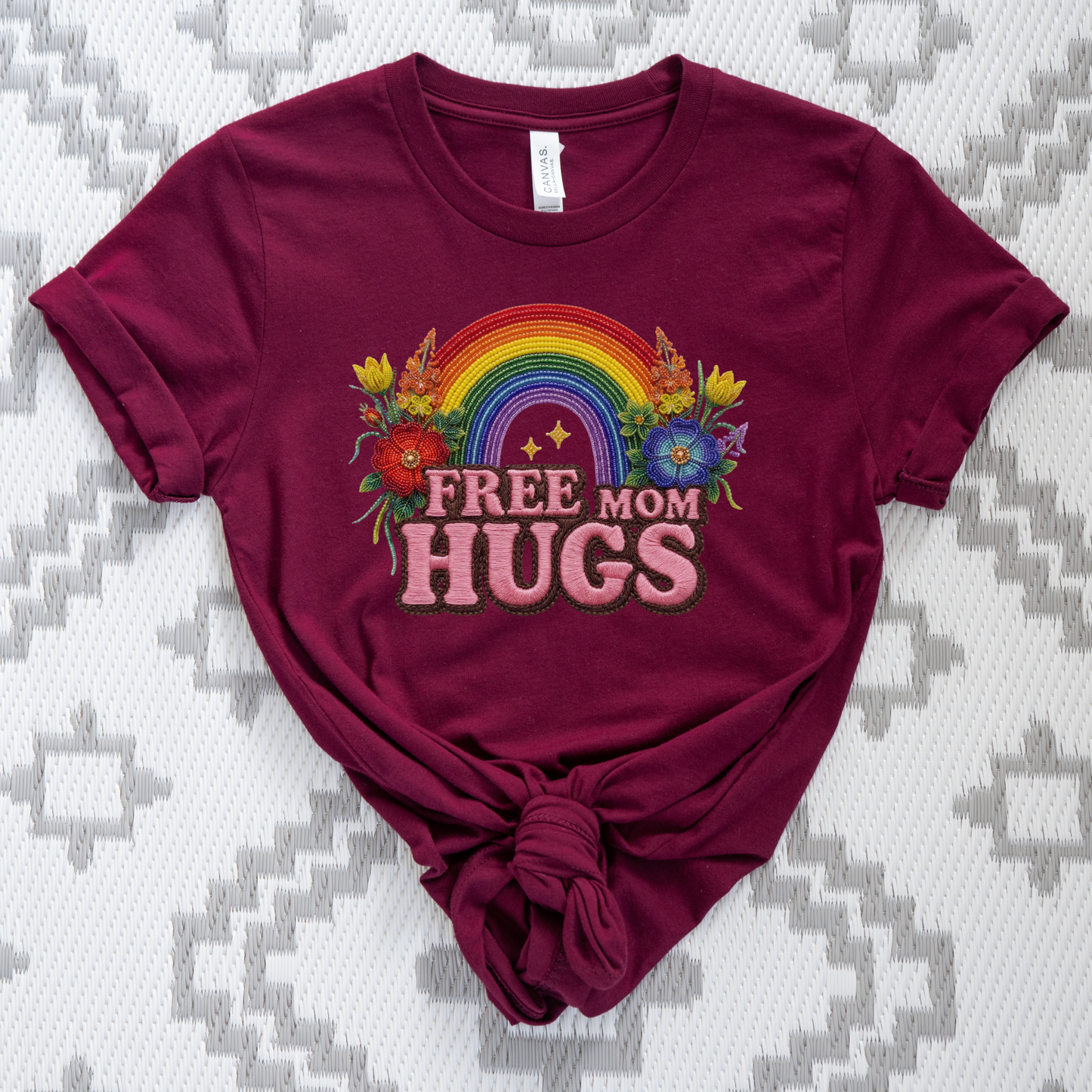 Free Mom Hugs Shirt featuring Indigenous-inspired beaded floral artwork, rainbow design, and pink faux embroidered lettering. free mom hugs shirt, pride shirt, indigenous floral shirt, beaded floral shirt, rainbow pride shirt, lgbtq ally shirt, supportive mom shirt, pride parade shirt, indigenous inspired apparel, faux embroidery shirt, mom hugs shirt, rainbow floral tee, inclusive apparel, pride month shirt, indigenous beadwork design, ally gift, lgbtq support shirt, community love shirt, acceptance shirt