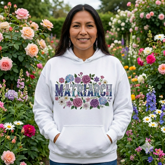 Woman wearing a white hoodie with 'Matriarch' and floral designs in a garden setting, Indigenous Woman Design