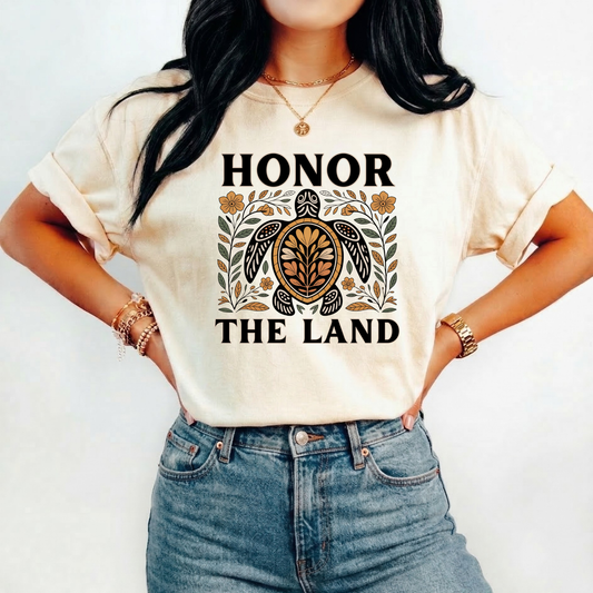 Person wearing a beige t-shirt with 'Honor the Land' design, honor the land turtle shirt, indigenous turtle floral shirt, indigenous designed turtle tee, land defender t-shirt, turtle symbolism indigenous apparel, floral turtle graphic tee, indigenous environmental shirt, honor the land tee, unisex indigenous shirt, indigenous owned clothing brand, cultural pride turtle shirt
