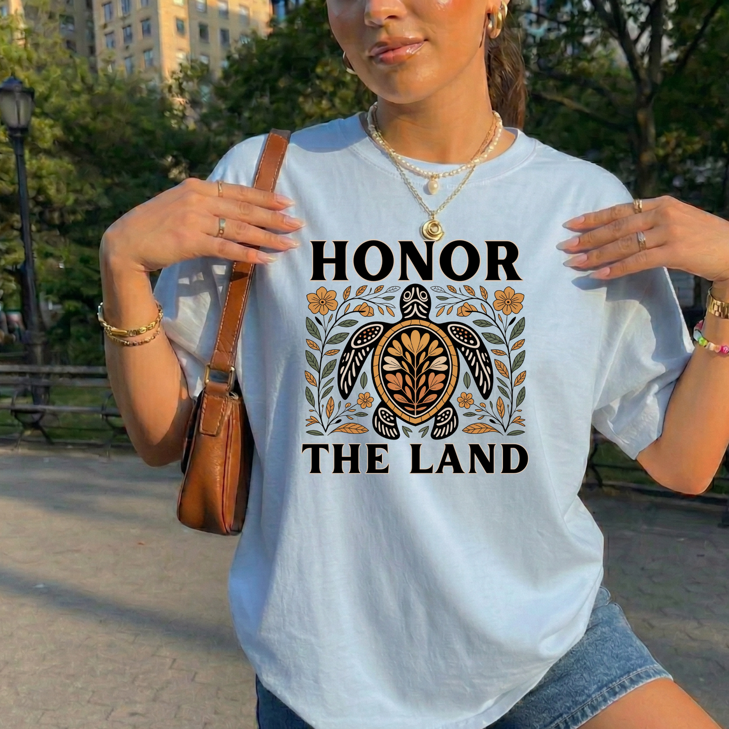 Person wearing a blue t-shirt with 'Honor the Land' design, honor the land turtle shirt, indigenous turtle floral shirt, indigenous designed turtle tee, land defender t-shirt, turtle symbolism indigenous apparel, floral turtle graphic tee, indigenous environmental shirt, honor the land tee, unisex indigenous shirt, indigenous owned cl