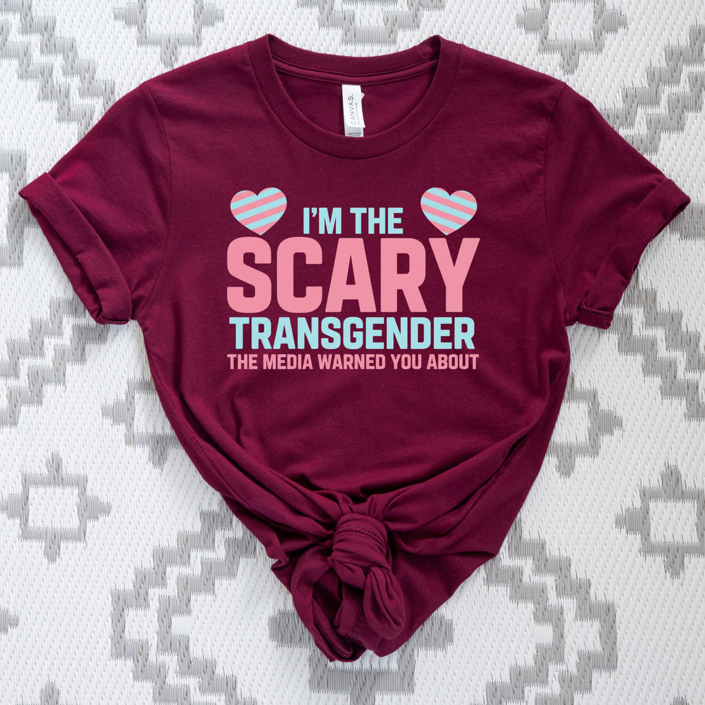 Maroon t-shirt with pink and blue text on a patterned background. transgender pride shirt, transgender t-shirt, LGBTQ+ clothing, trans visibility apparel, equality shirt, pride shirt for adults, trans rights clothing, LGBTQ pride tee, gender identity shirt, inclusive fashion, queer clothing brand, pride month outfit, unisex pride shirt, trans empowerment shirt, activism apparel