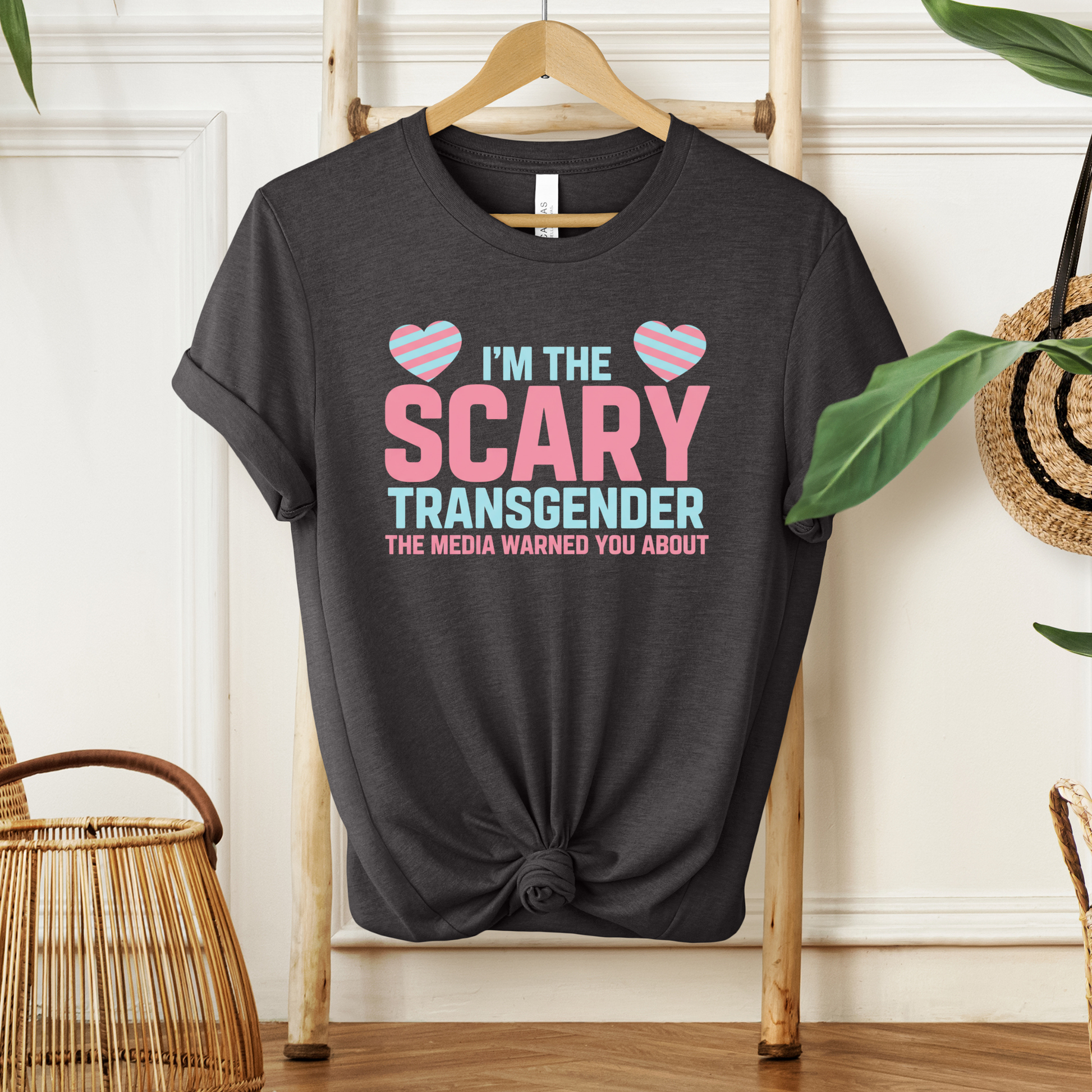 Black t-shirt with pink and blue text on a hanger against a white wall. transgender pride shirt, transgender t-shirt, LGBTQ+ clothing, trans visibility apparel, equality shirt, pride shirt for adults, trans rights clothing, LGBTQ pride tee, gender identity shirt, inclusive fashion, queer clothing brand, pride month outfit, unisex pride shirt, trans empowerment shirt, activism apparel