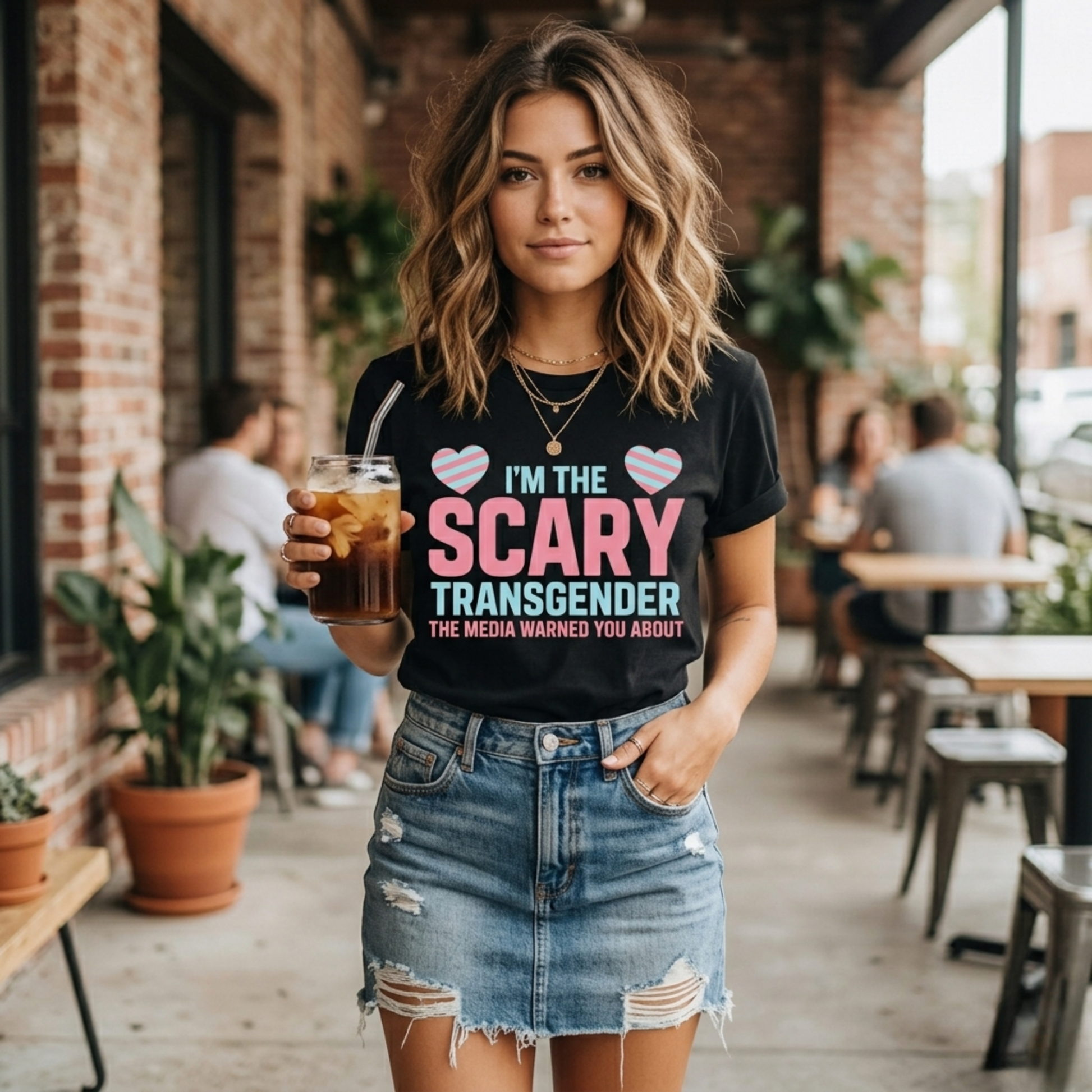Woman wearing a black t-shirt with a message, holding a drink in an outdoor cafe setting. transgender pride shirt, transgender t-shirt, LGBTQ+ clothing, trans visibility apparel, equality shirt, pride shirt for adults, trans rights clothing, LGBTQ pride tee, gender identity shirt, inclusive fashion, queer clothing brand, pride month outfit, unisex pride shirt, trans empowerment shirt, activism apparel