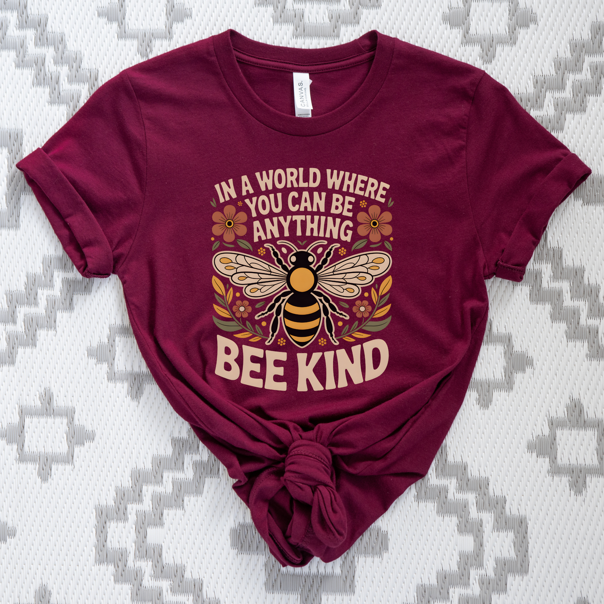 Maroon t-shirt with bee graphic and 'Bee Kind' text on a patterned background. bee kind shirt, indigenous designed shirt, floral bee shirt, kindness shirt, inspirational t shirt, nature inspired clothing, positive message shirt, indigenous art shirt, graphic tee, unisex t shirt, gift for her, uplifting apparel