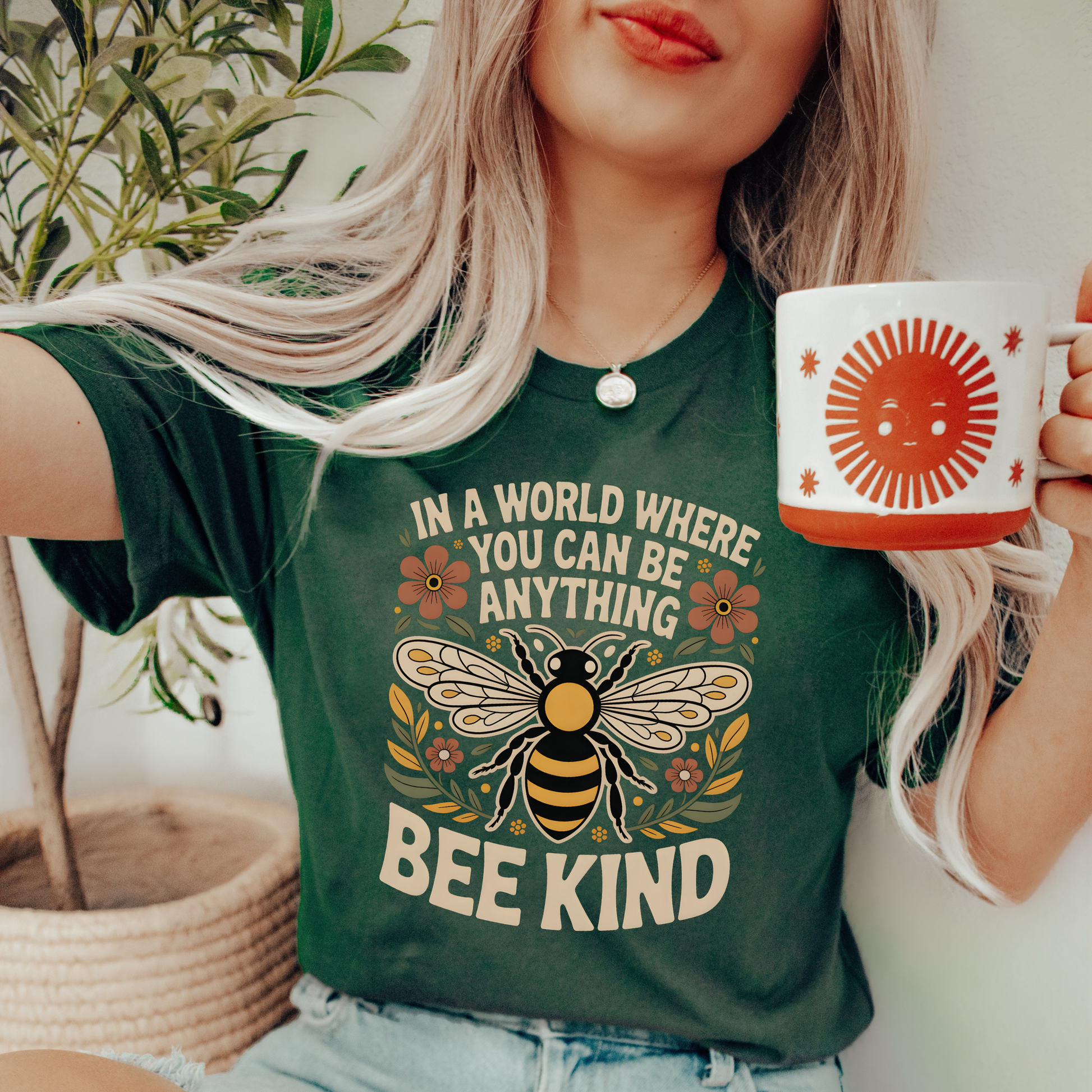 Person wearing a green t-shirt with a bee design and 'Bee Kind' text, holding a mug. bee kind shirt, indigenous designed shirt, floral bee shirt, kindness shirt, inspirational t shirt, nature inspired clothing, positive message shirt, indigenous art shirt, graphic tee, unisex t shirt, gift for her, uplifting apparel