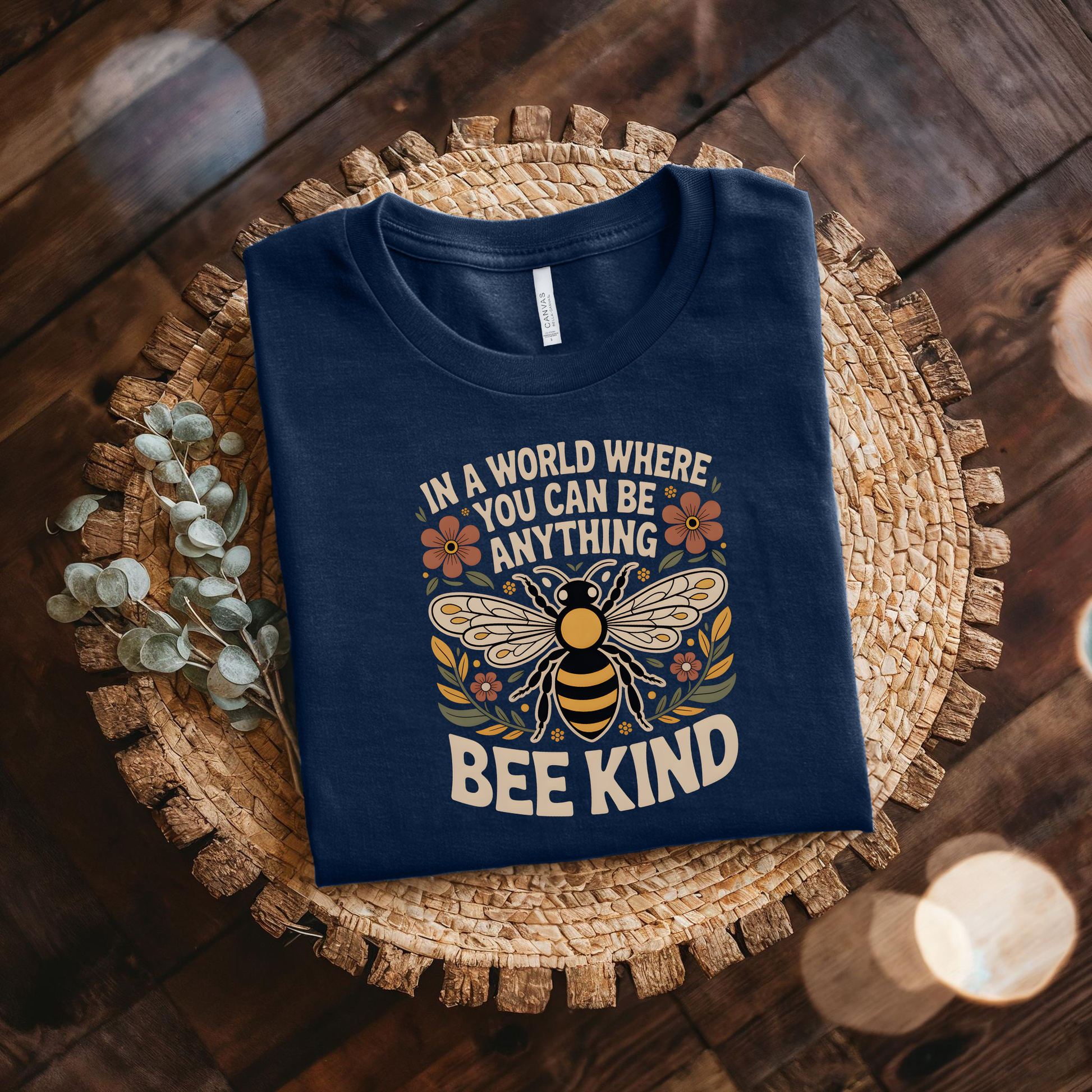 Folded navy blue t-shirt with bee design and text on a woven mat. bee kind shirt, indigenous designed shirt, floral bee shirt, kindness shirt, inspirational t shirt, nature inspired clothing, positive message shirt, indigenous art shirt, graphic tee, unisex t shirt, gift for her, uplifting apparel