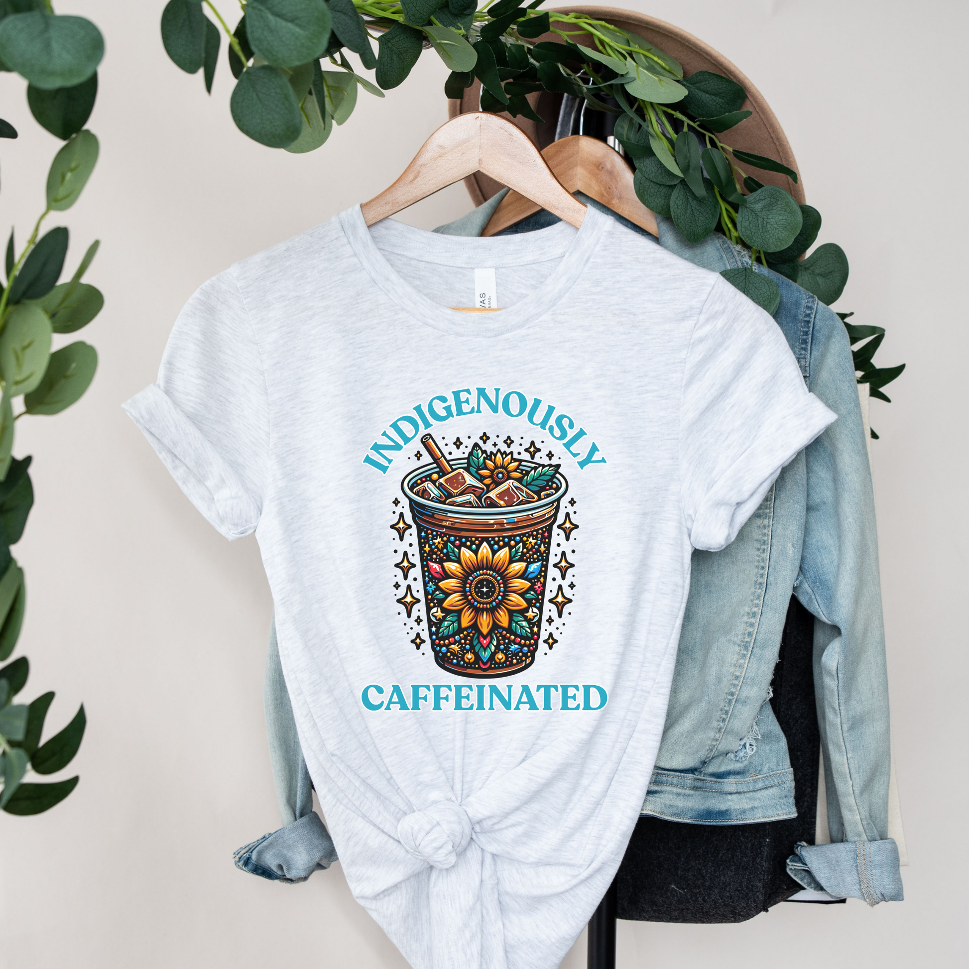 t-shirt featuring a vibrant Indigenous-inspired floral iced coffee design with the phrase "Indigenously Caffeinated" in turquoise lettering. indigenously caffeinated shirt, indigenous coffee lover shirt, indigenous graphic tee, native coffee shirt, coffee lover apparel, indigenous pride clothing, floral coffee design shirt, indigenous entrepreneur shirt, caffeine lover gift, indigenous fashion canada, indigenous art t-shirt, iced coffee graphic tee, indigenous gift ideas, coffee addict shirt, indigenous sma