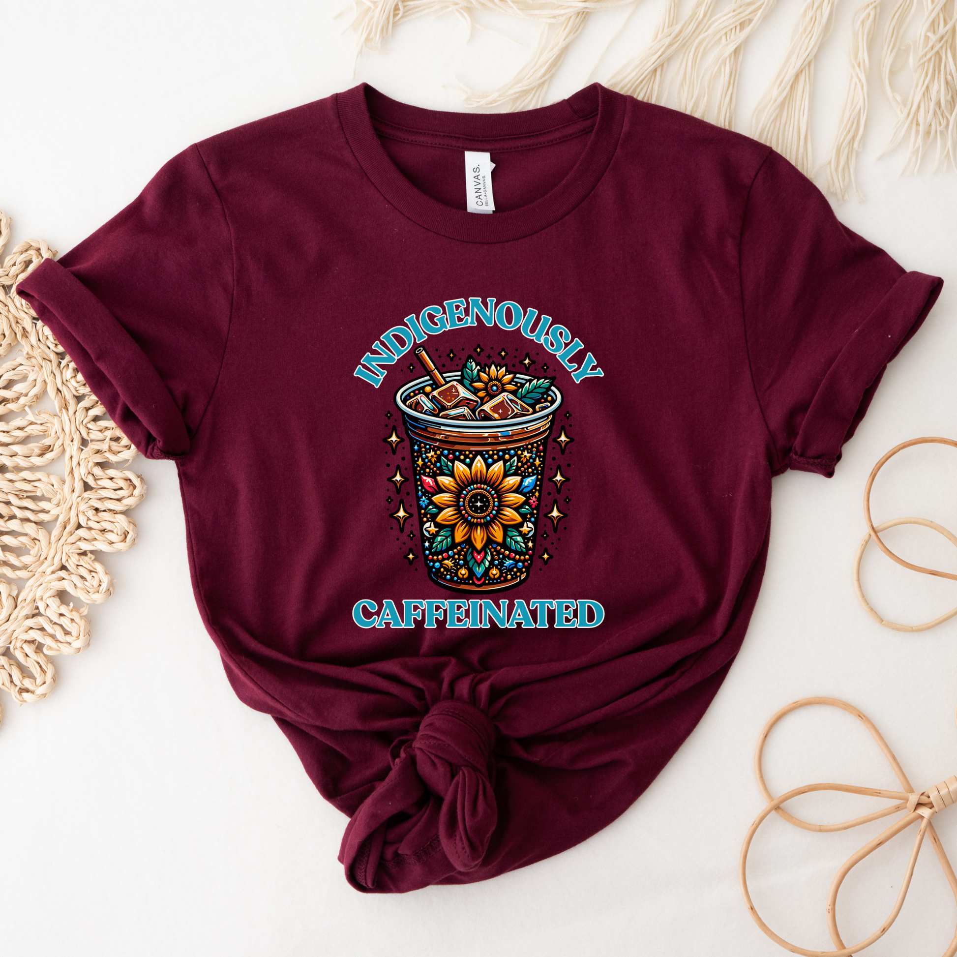 t-shirt featuring a vibrant Indigenous-inspired floral iced coffee design with the phrase "Indigenously Caffeinated" in turquoise lettering. indigenously caffeinated shirt, indigenous coffee lover shirt, indigenous graphic tee, native coffee shirt, coffee lover apparel, indigenous pride clothing, floral coffee design shirt, indigenous entrepreneur shirt, caffeine lover gift, indigenous fashion canada, indigenous art t-shirt, iced coffee graphic tee, indigenous gift ideas, coffee addict shirt, indigenous sma