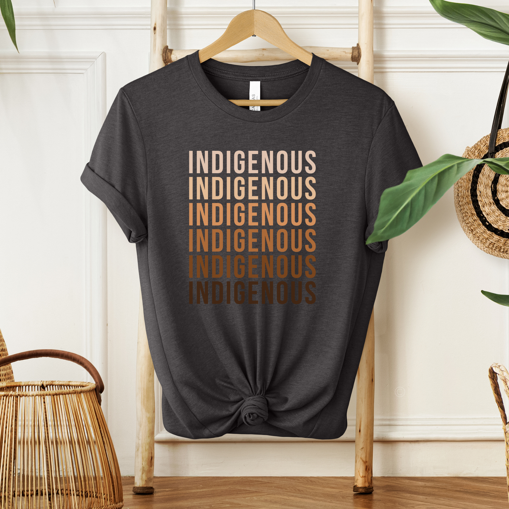 Black t-shirt with floral design and text on a wooden hanger against a white wall. Indigenous shirt, Indigenous repeated words shirt, Indigenous pride, Native apparel, Indigenous graphic tee, statement shirt, unisex t shirt, bold typography shirt, Indigenous identity, cultural pride tee, Indigenous clothing, modern graphic tee, awareness shirt, Native inspired fashion, everyday tee
