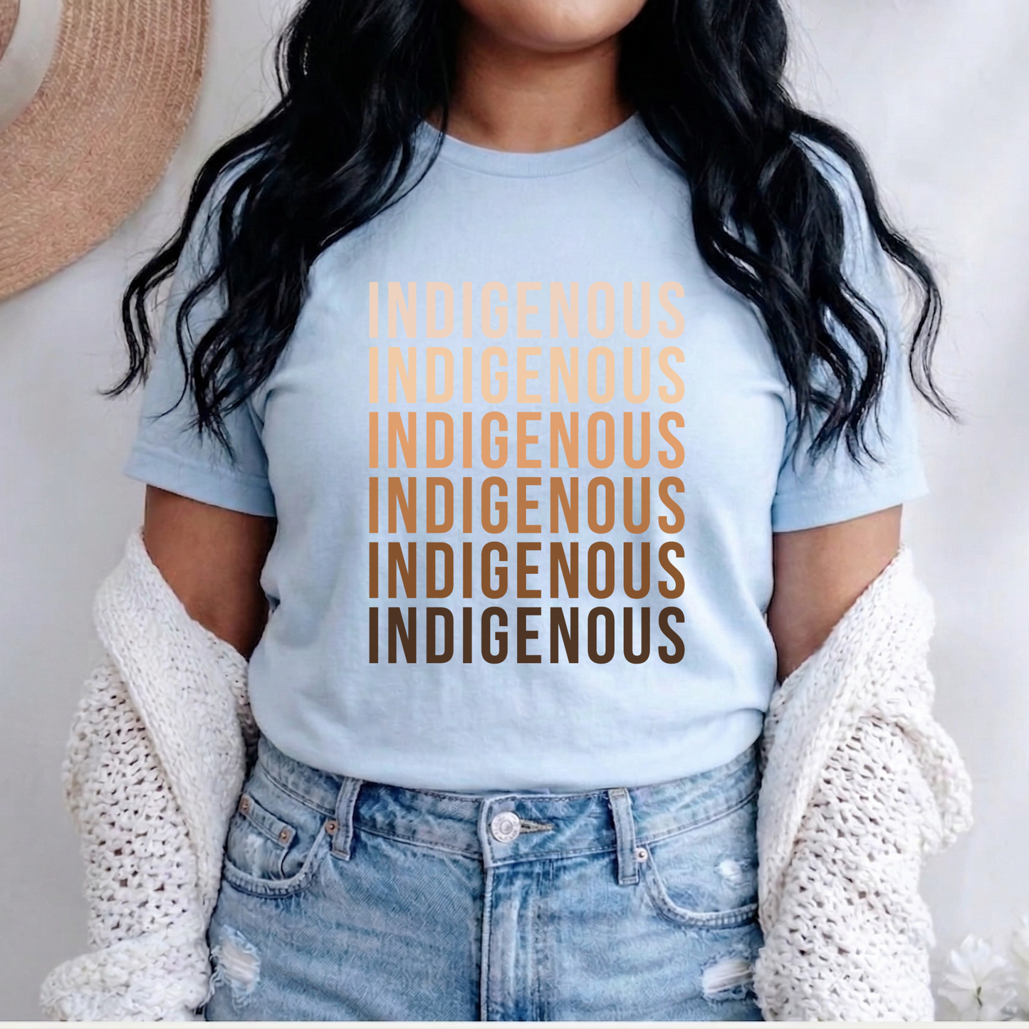 Person wearing a light blue t-shirt with 'Indigenous' printed multiple times in brown. Indigenous shirt, Indigenous repeated words shirt, Indigenous pride, Native apparel, Indigenous graphic tee, statement shirt, unisex t shirt, bold typography shirt, Indigenous identity, cultural pride tee, Indigenous clothing, modern graphic tee, awareness shirt, Native inspired fashion, everyday tee