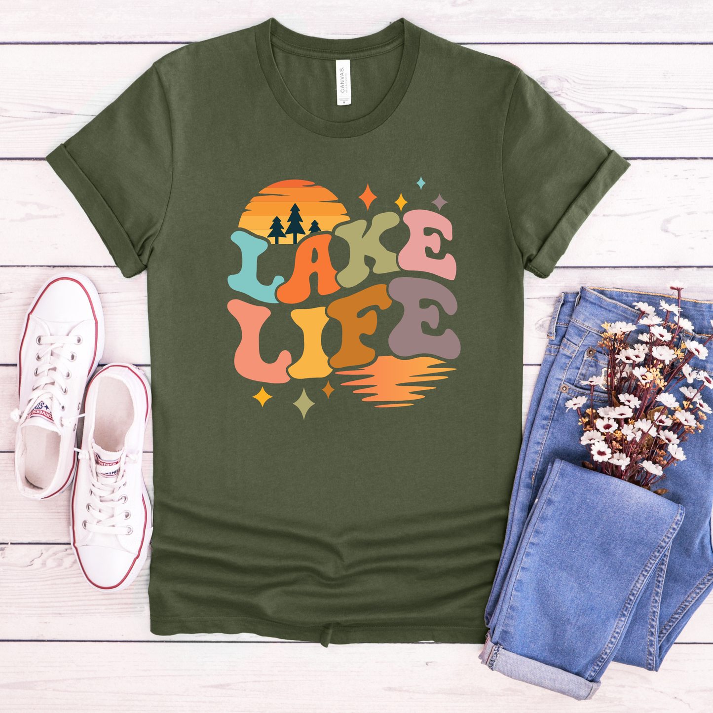 Green t-shirt with 'Lake Life' design on a wooden surface with jeans and sneakers. lake life shirt, lake life tee, retro lake graphic shirt, sunset lake shirt, boating shirt, lake lover apparel, summer lake tee, unisex lake life clothing, lake house gift, fishing shirt, cottage lake outfit, lake vacation tee, boater shirt, lakeside apparel, retro sunset graphic tee