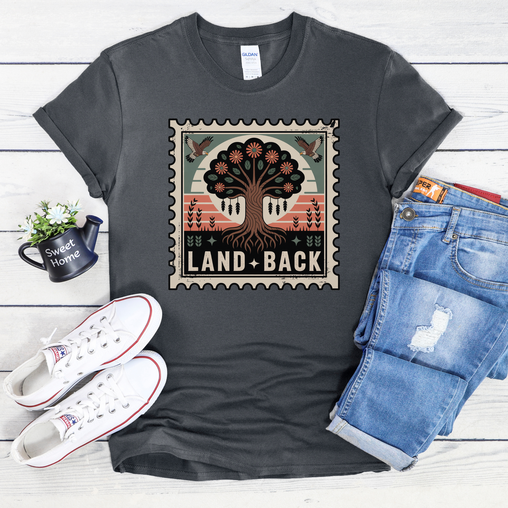 Gray t-shirt with a graphic design featuring a tree and 'Land Back' text, displayed with white sneakers and blue jeans on a wooden surface. land back shirt, indigenous awareness shirt, nature shirt, tree graphic tee, minimalist shirt, advocacy apparel, eco conscious clothing, indigenous inspired apparel, social justice shirt, unisex t shirt, earthy aesthetic clothing, statement tee