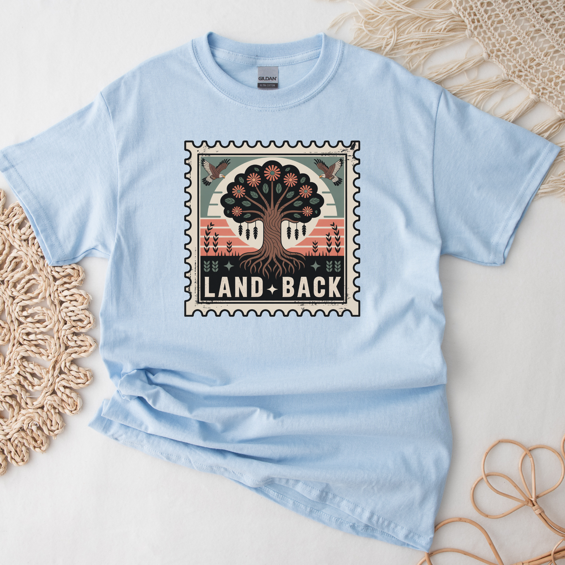 Light blue t-shirt with a graphic design featuring a tree and 'Land Back' text on a textured surface. land back shirt, indigenous awareness shirt, nature shirt, tree graphic tee, minimalist shirt, advocacy apparel, eco conscious clothing, indigenous inspired apparel, social justice shirt, unisex t shirt, earthy aesthetic clothing, statement tee