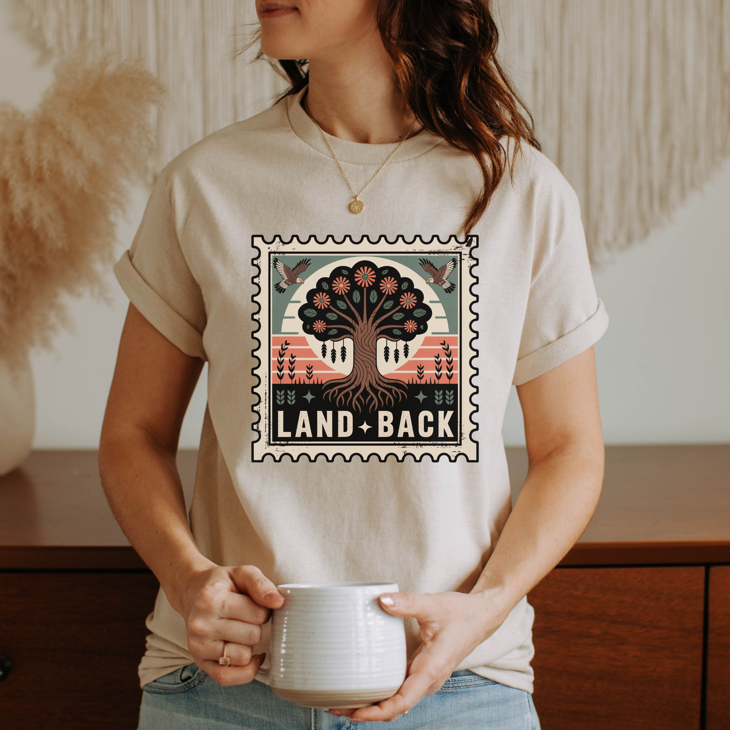 Person wearing a t-shirt with a tree design and 'Land Back' text, holding a mug. land back shirt, indigenous awareness shirt, nature shirt, tree graphic tee, minimalist shirt, advocacy apparel, eco conscious clothing, indigenous inspired apparel, social justice shirt, unisex t shirt, earthy aesthetic clothing, statement tee
